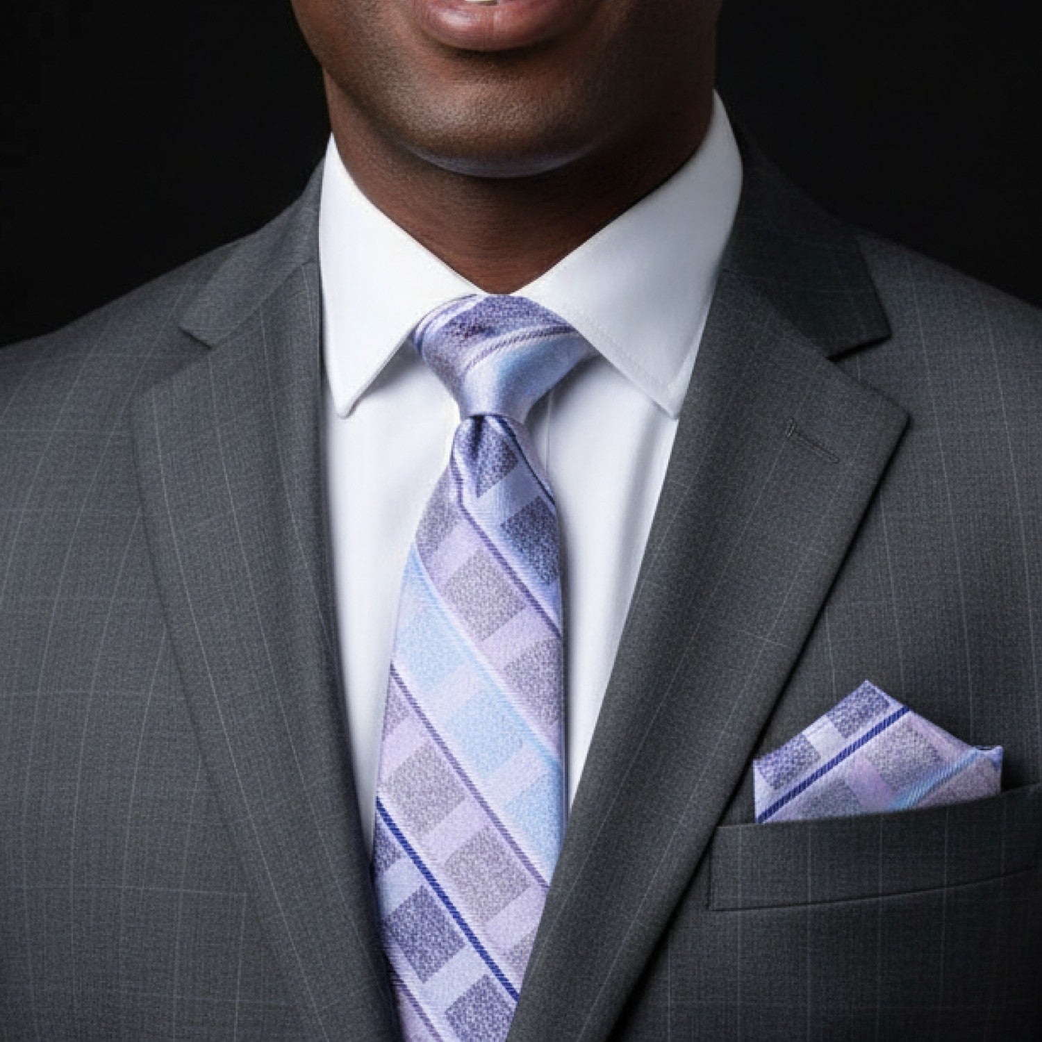 Man wearing a gray suit with a patterned tie and pocket square on a black background