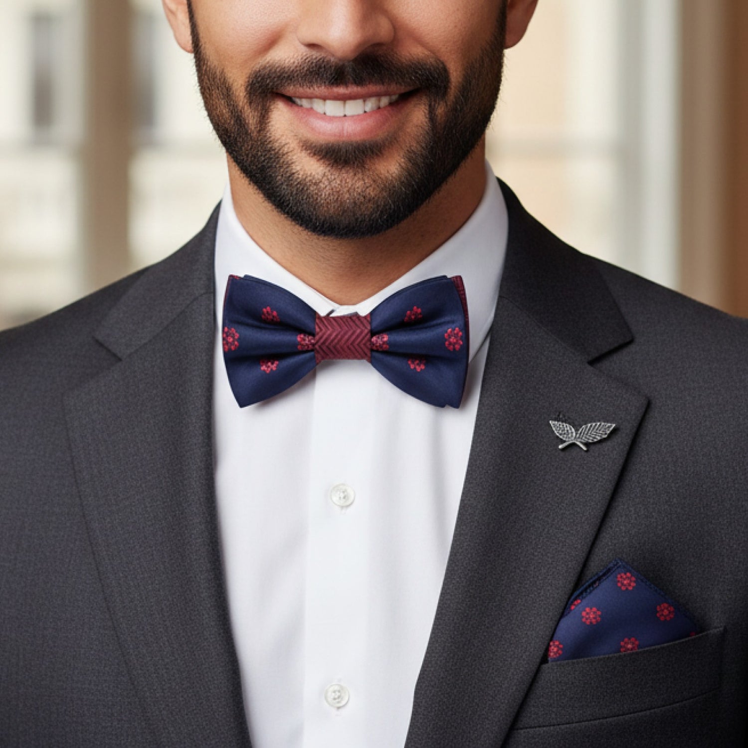 Man wearing a gray suit with a navy bow tie and pocket square, smiling.