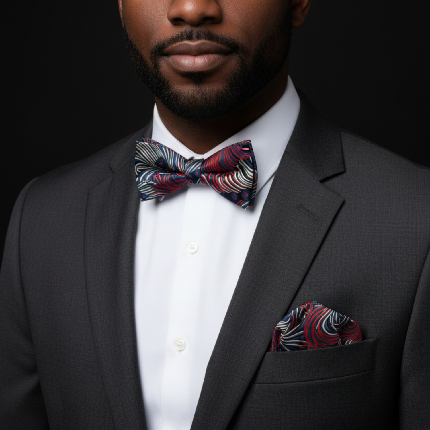 Man wearing a dark suit with a colorful bow tie and pocket square against a black background