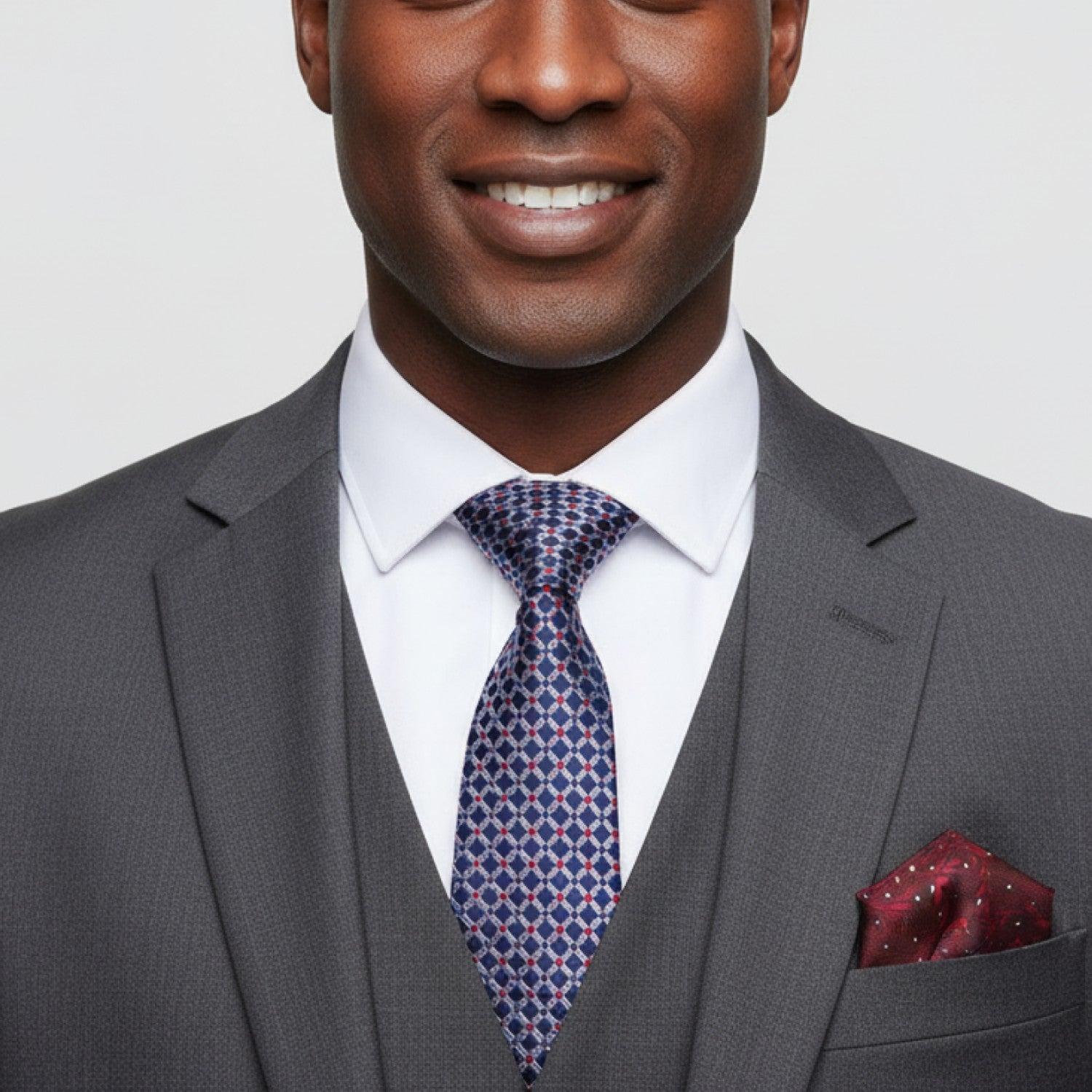 Man wearing a gray suit with a patterned tie and pocket square on a light gray background