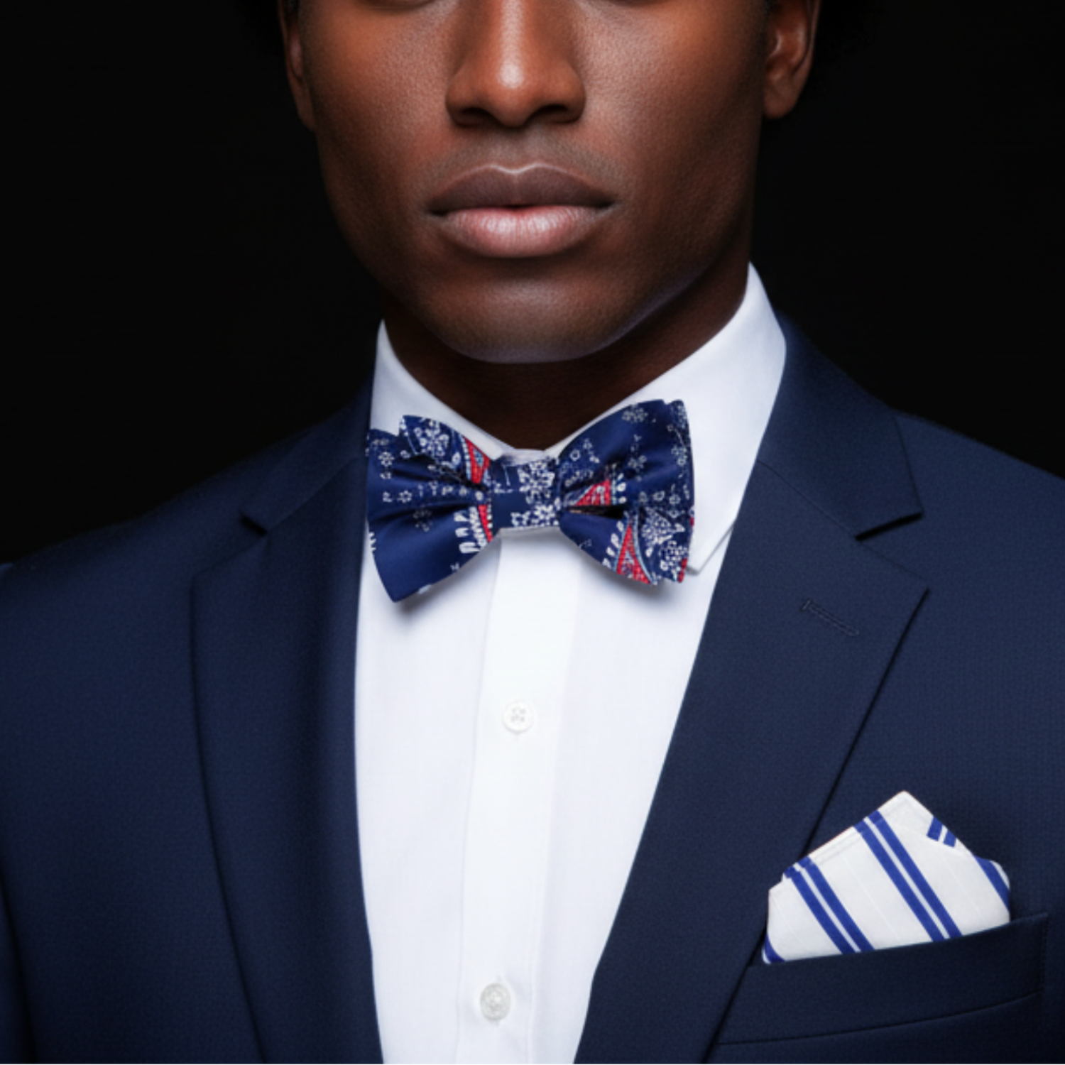 Man wearing a navy suit with a patterned bow tie and pocket square against a black background