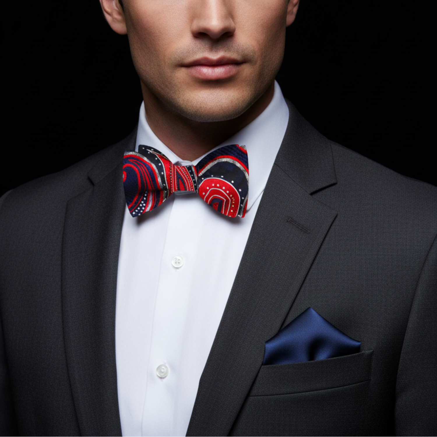 Man wearing a black suit with a red, white, and blue patterned bow tie against a black background