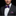 Man wearing a black suit with a white shirt, purple bow tie with red polka dots, and matching pocket square on a black background.