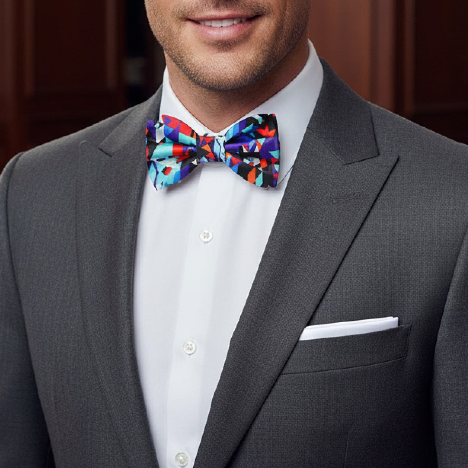 Man wearing a gray suit with a colorful bow tie and white pocket square.