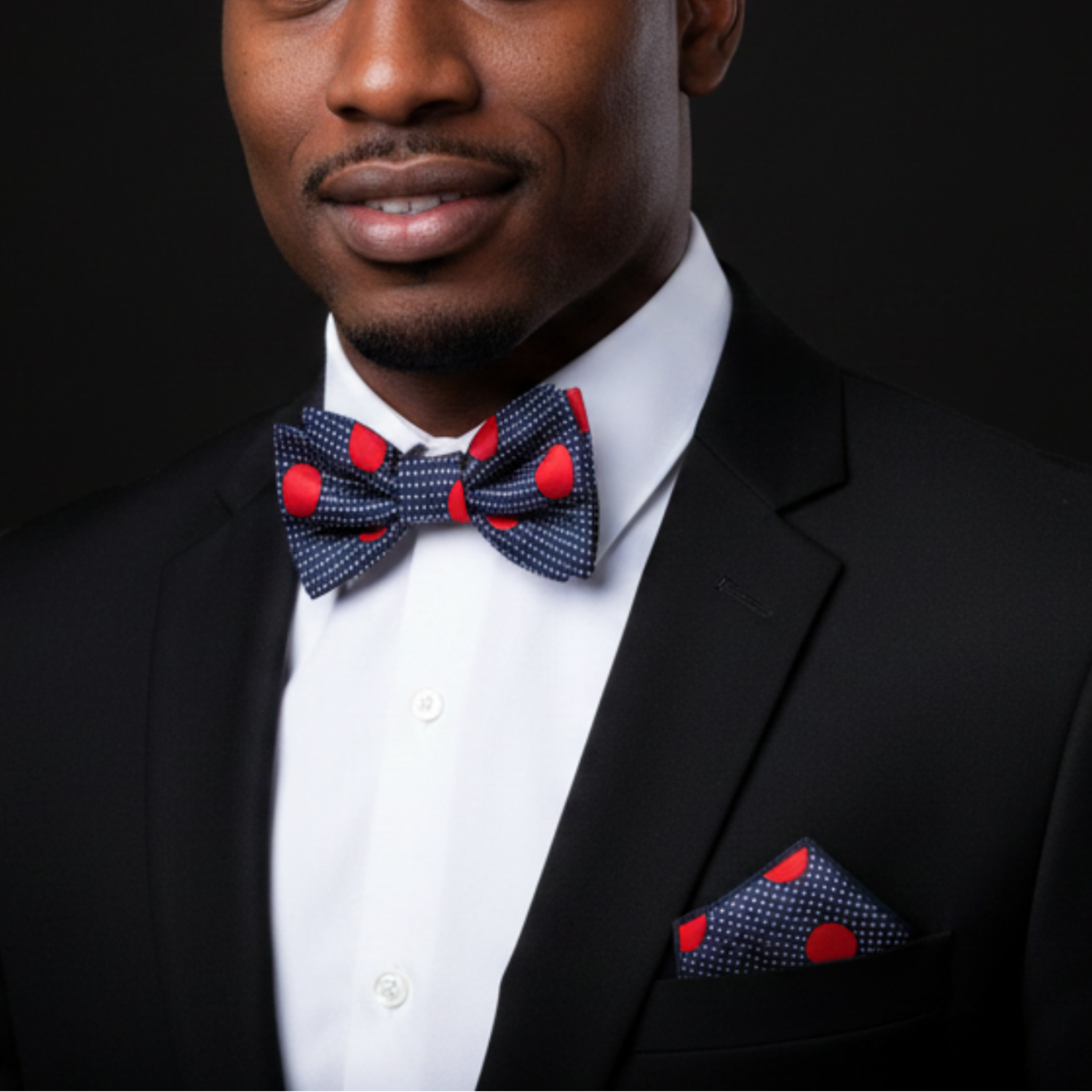 Man wearing a black suit with a red and blue bow tie and pocket square against a dark background