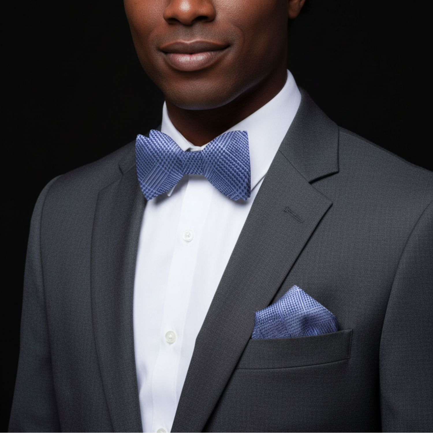 Man wearing a gray suit with a blue bow tie and pocket square on a black background