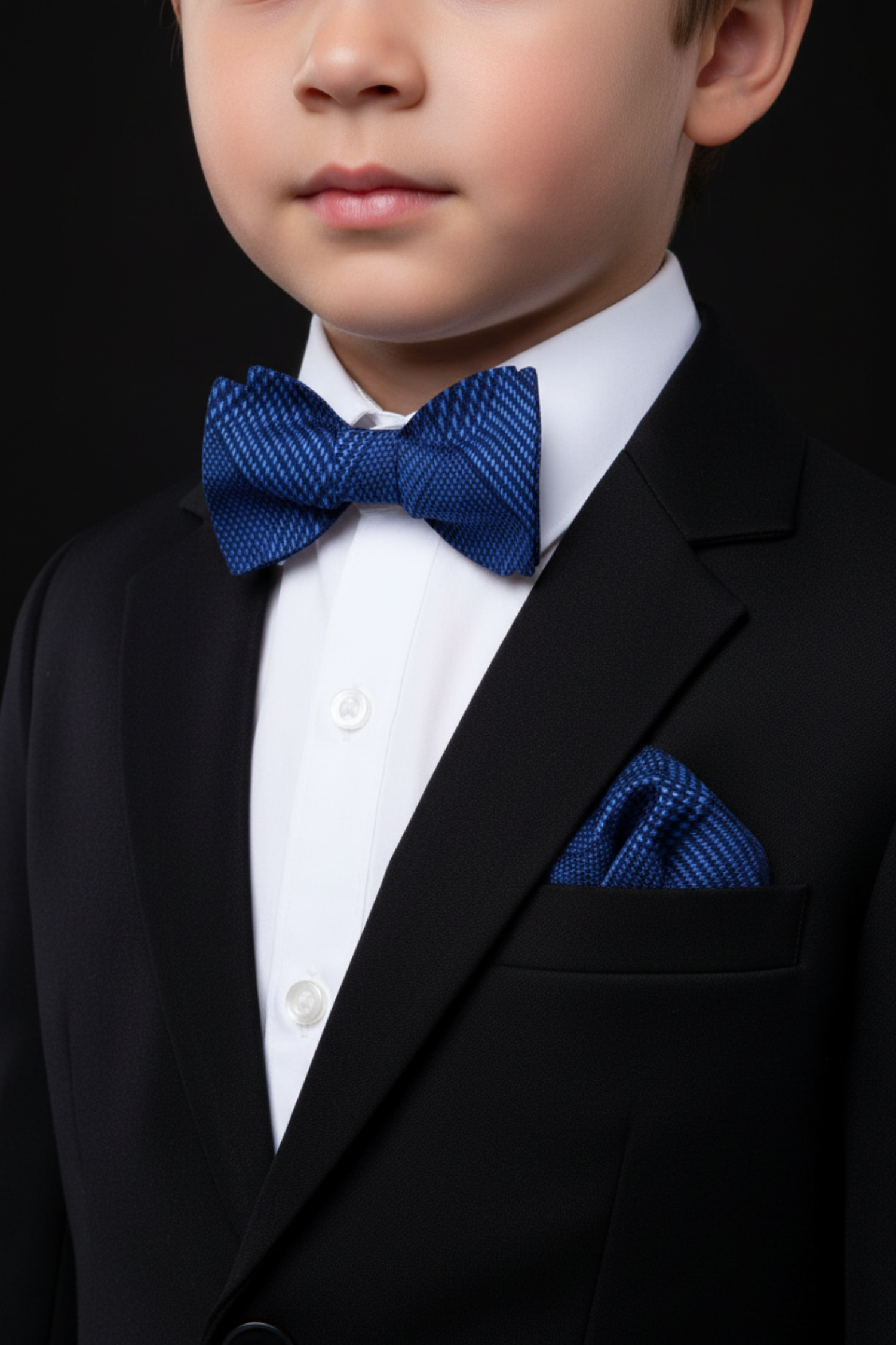 Young boy in a formal outfit with a blue bow tie and pocket square on a black background