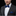 Man wearing a black suit with a white shirt and blue bow tie and pocket square on a black background