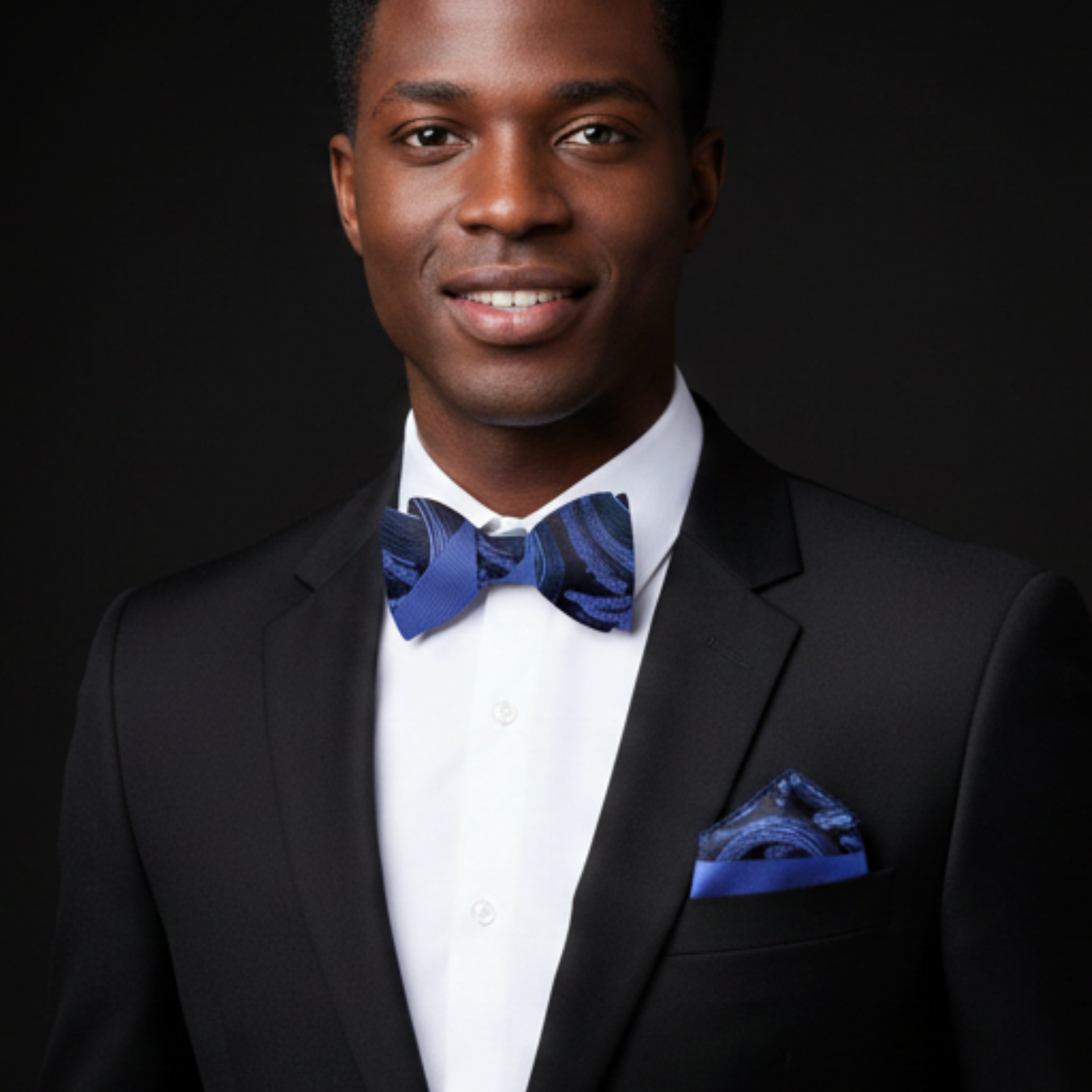 Man wearing a black suit with a blue bow tie and pocket square against a dark background
