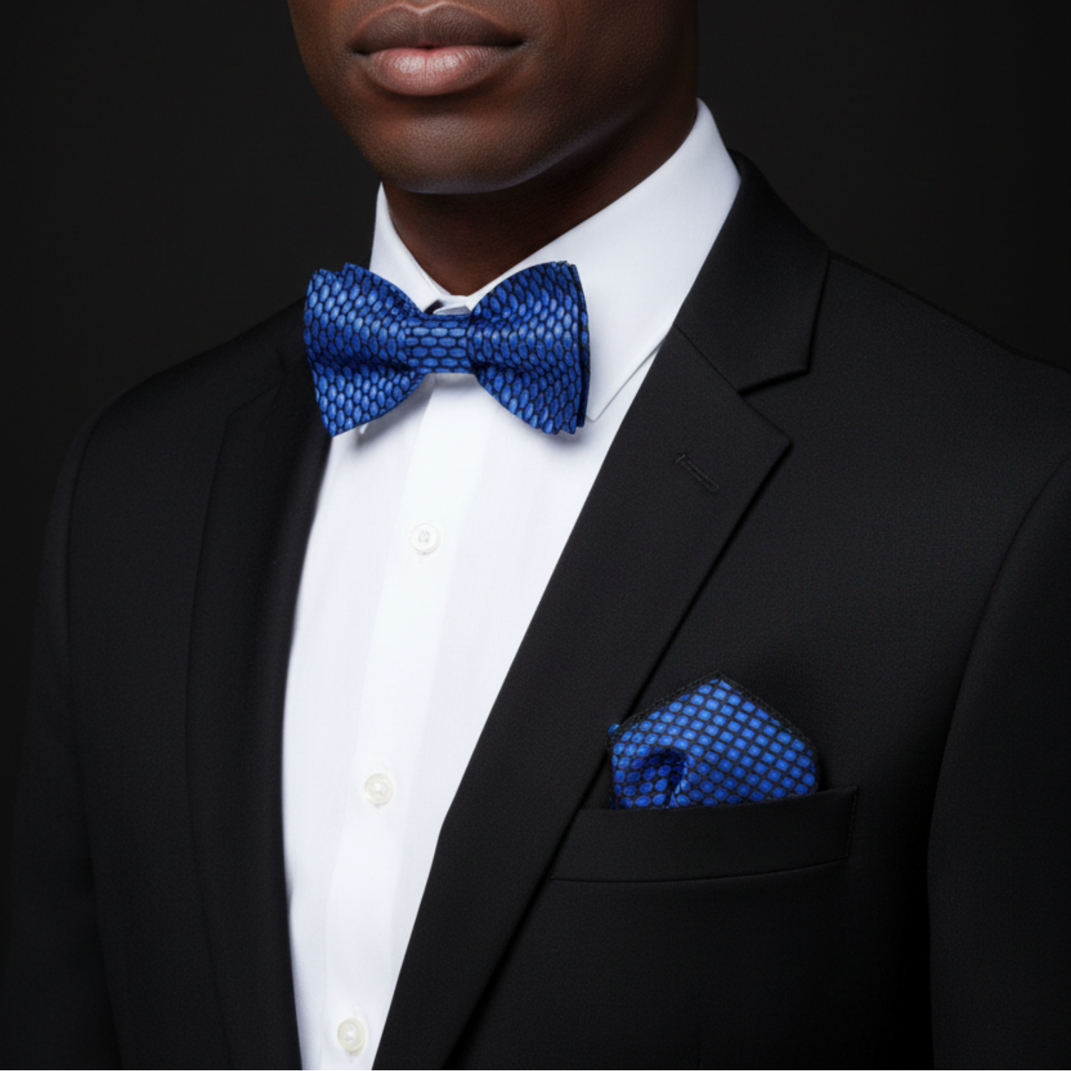 Man wearing a black suit with a blue bow tie and pocket square on a dark background