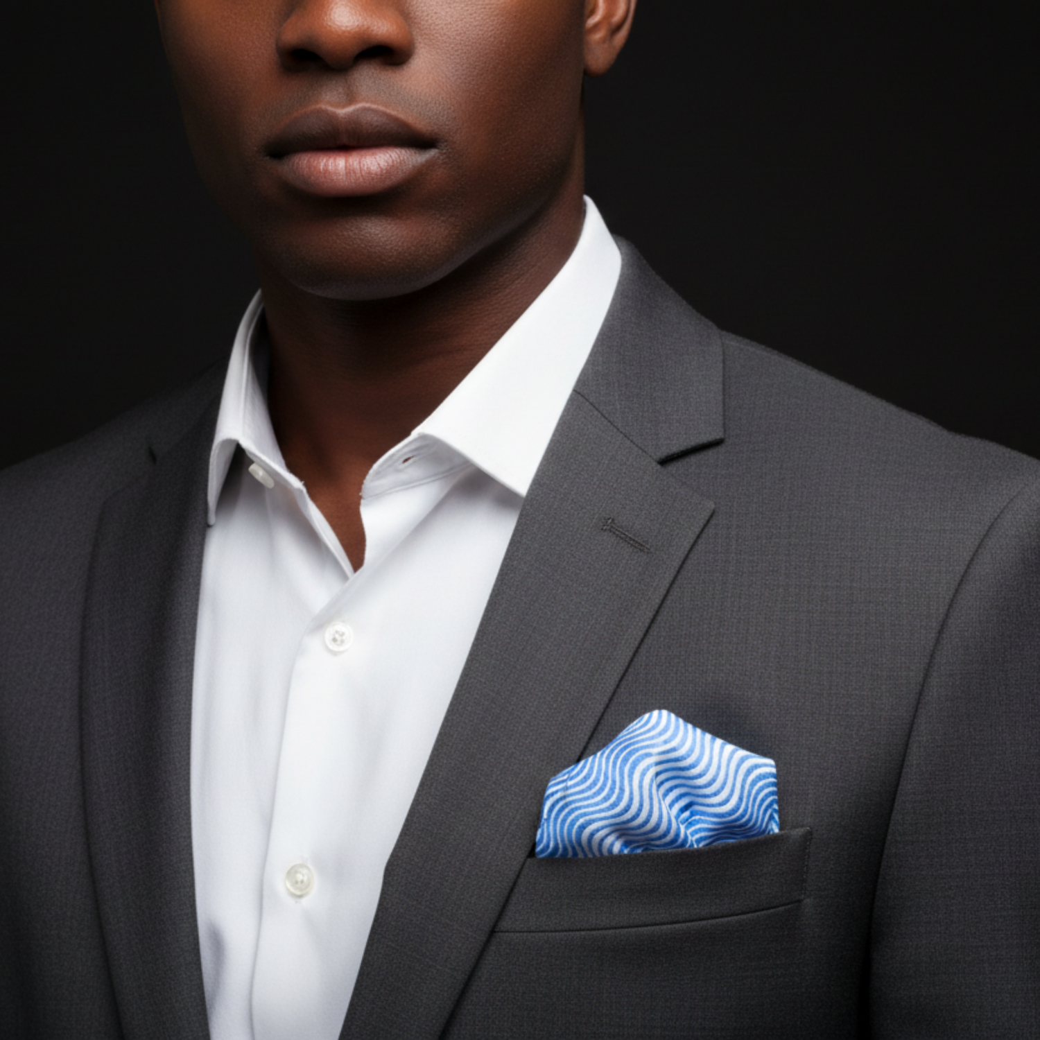 Man wearing a dark suit with a white shirt and blue patterned pocket square on a black background