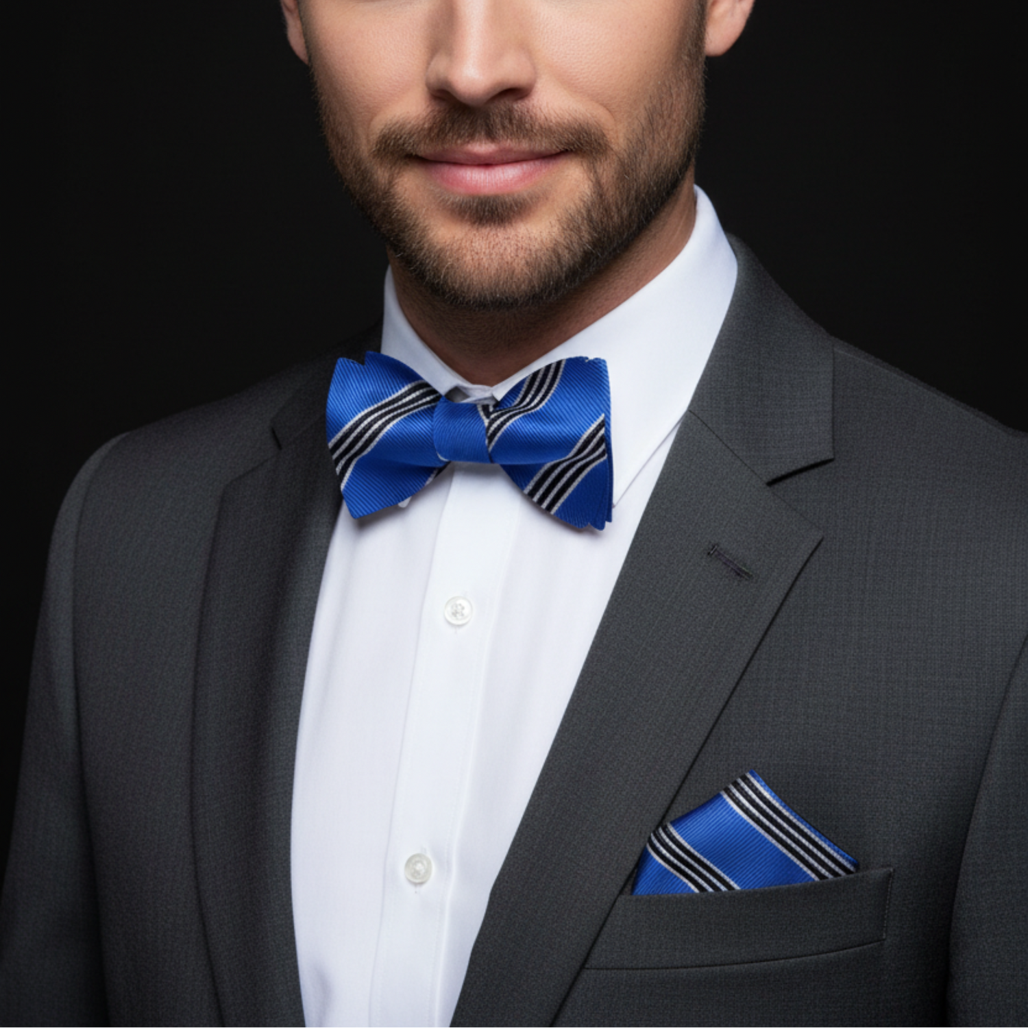 Man wearing a gray suit with a blue bow tie and pocket square on a black background