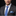 Man wearing a gray suit with a blue patterned tie and pocket square on a black background