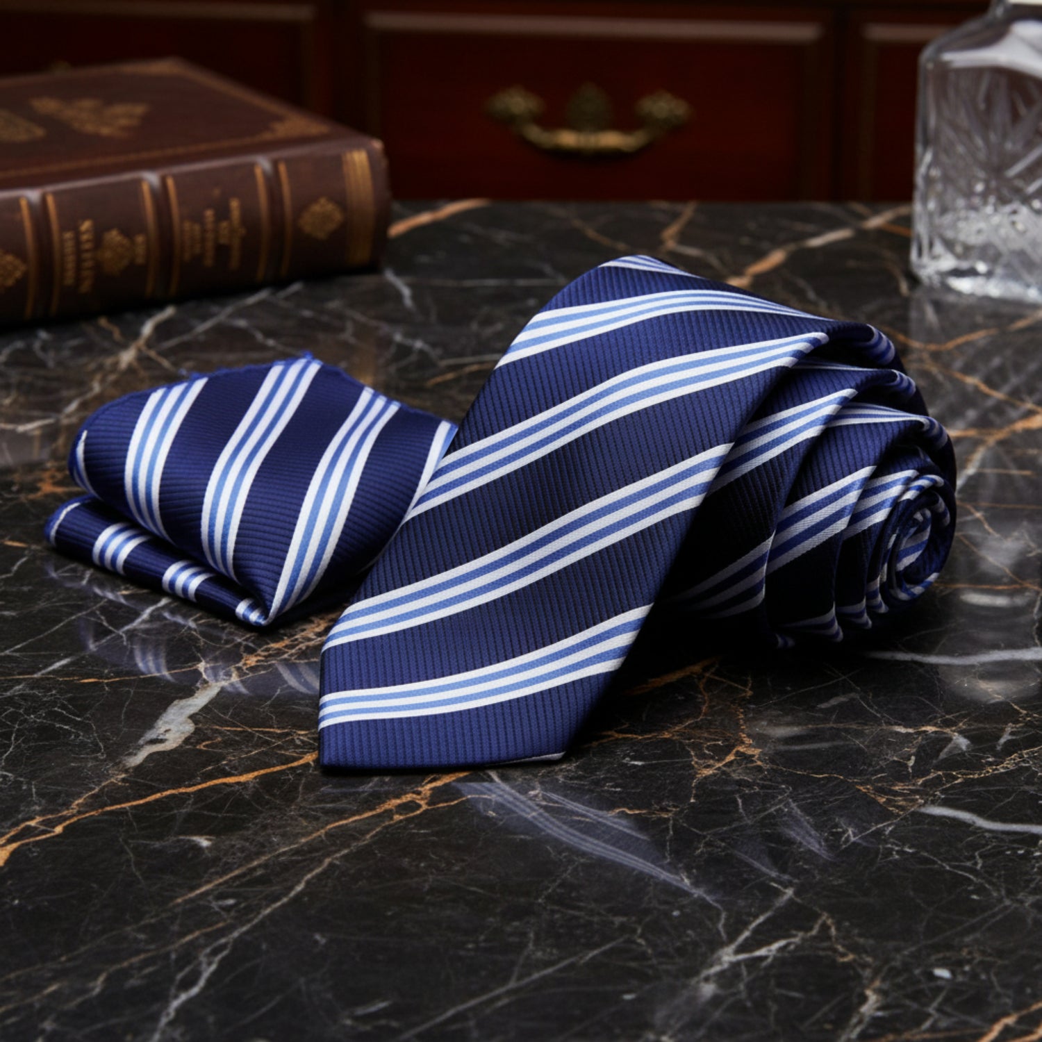 Navy blue tie with white stripes and matching pocket square on a marble background