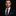 Man wearing a black suit with a blue polka dot tie and pocket square on a dark background