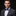 Man wearing a gray suit with a blue bow tie and patterned pocket square on a black background