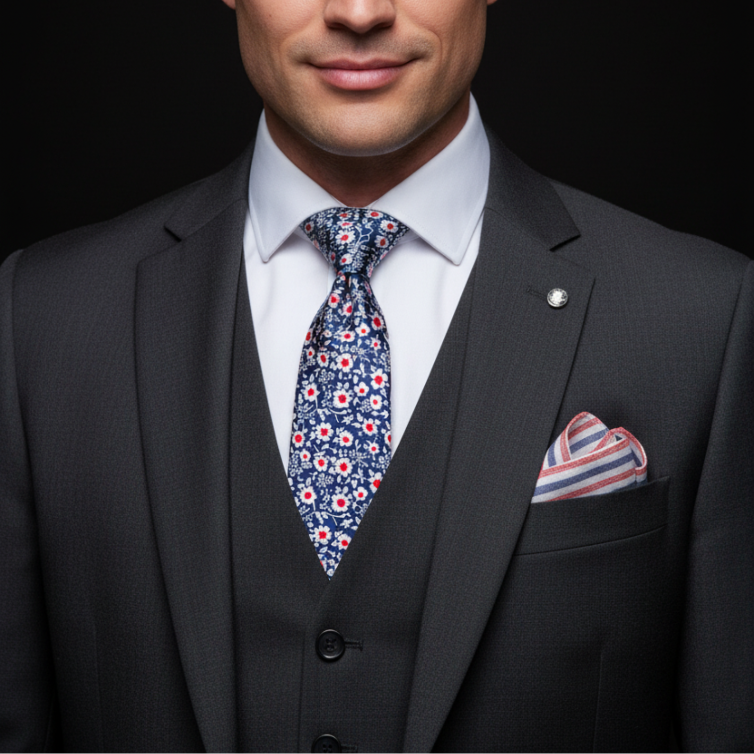 Man wearing a dark gray suit with a patterned tie and pocket square on a black background