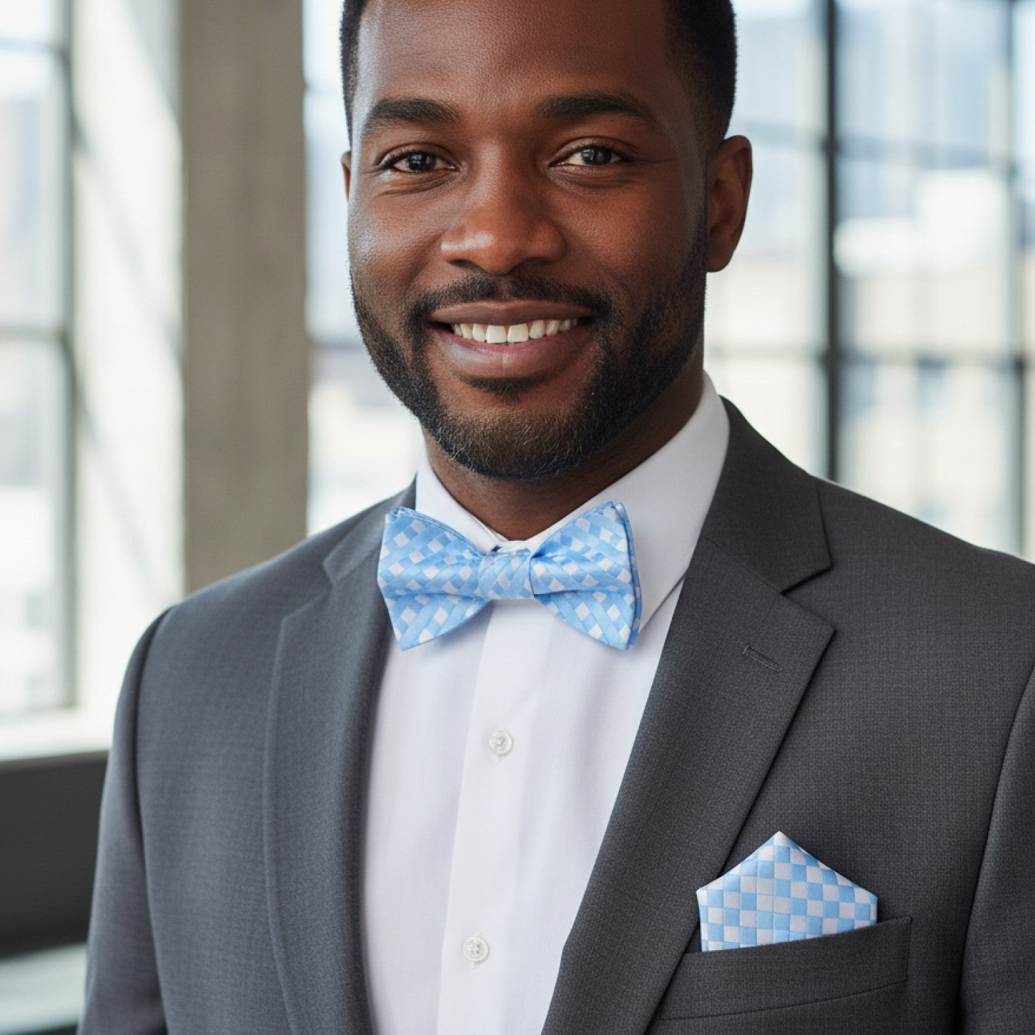 Man wearing a gray suit with a blue bow tie and pocket square indoors.