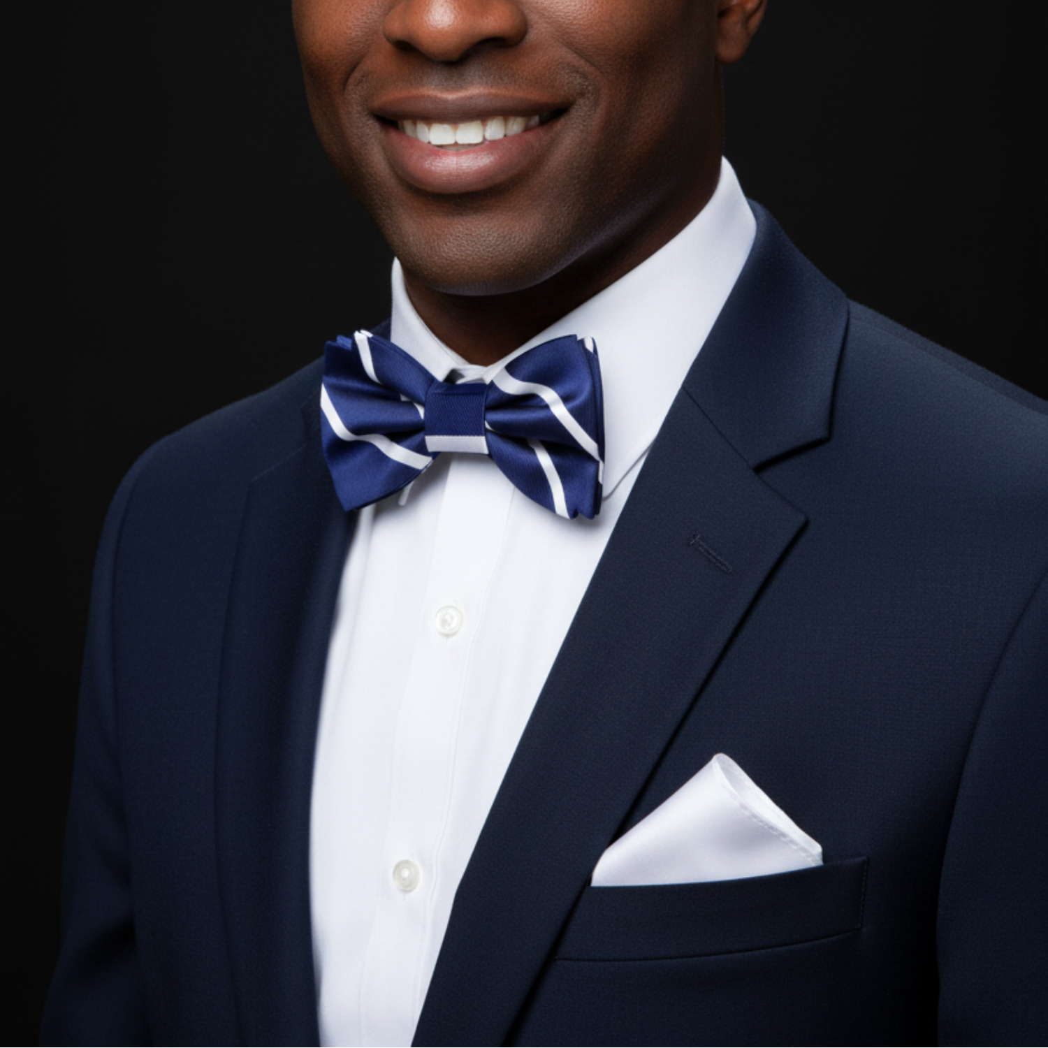Man wearing a navy suit with a white shirt and blue bow tie on a black background