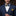 Man wearing a navy suit with a yellow pocket square and patterned bow tie against a blurred background.