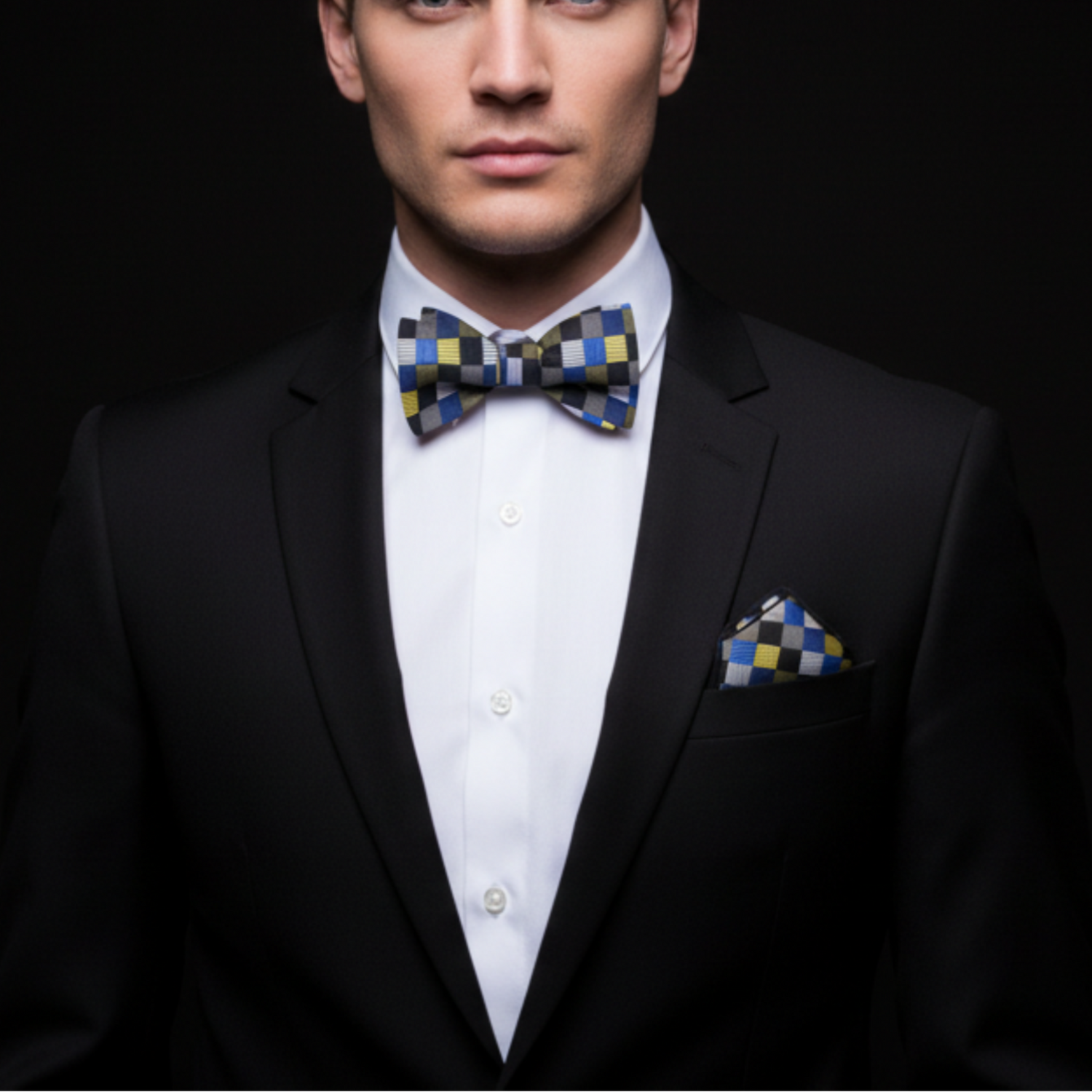 Man wearing a black suit with a checkered bow tie and pocket square on a dark background