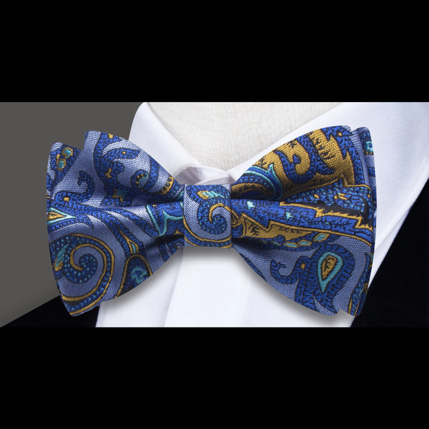 A paisley patterned bow tie in blue and yellow, displayed on a white background and paired with a matching pocket square.