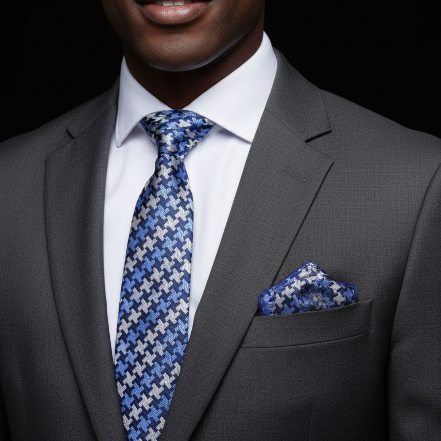 Man wearing a gray suit with a blue patterned tie and pocket square on a black background