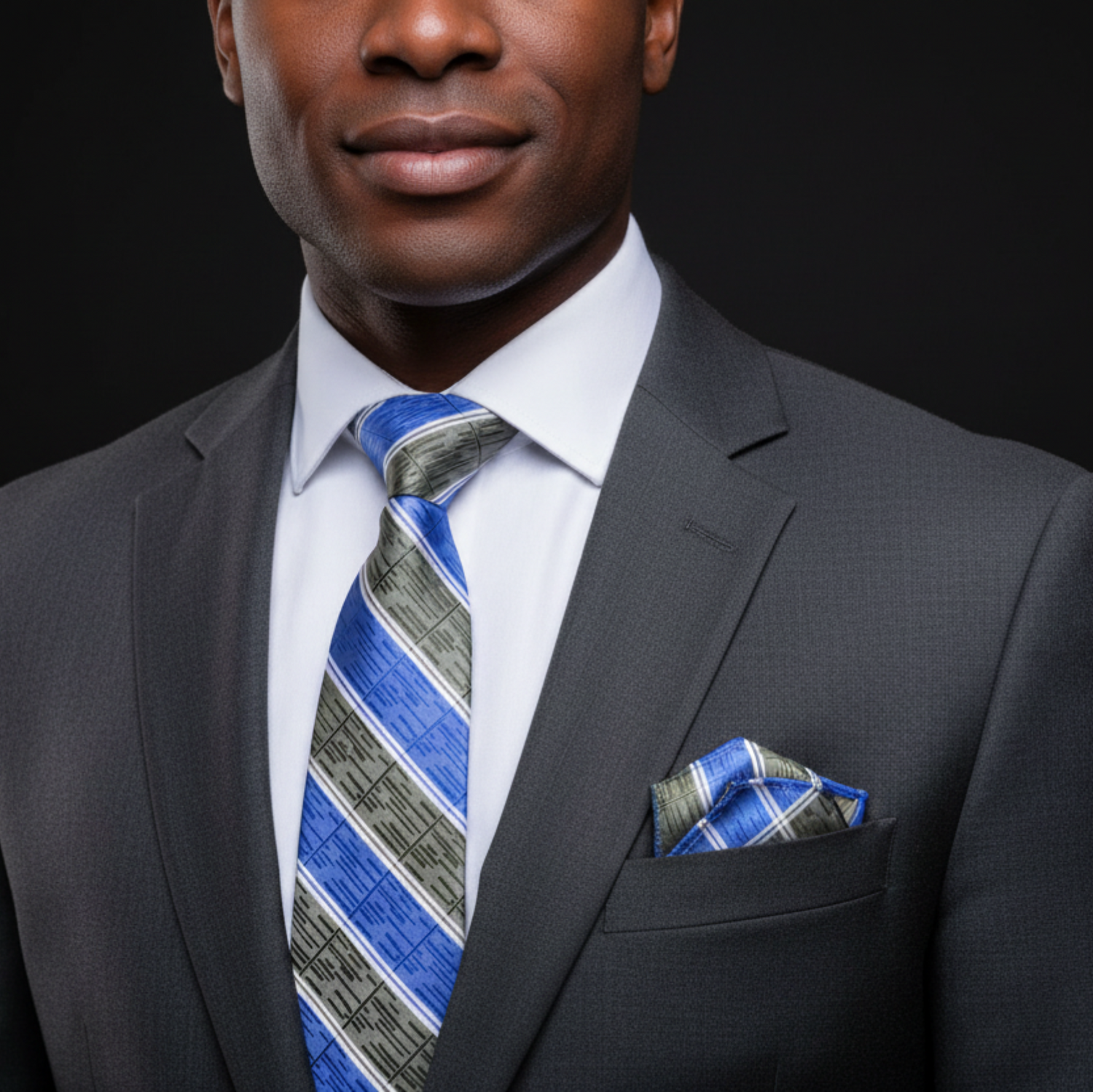 Man wearing a gray suit with a blue and gray striped tie and matching pocket square on a black background