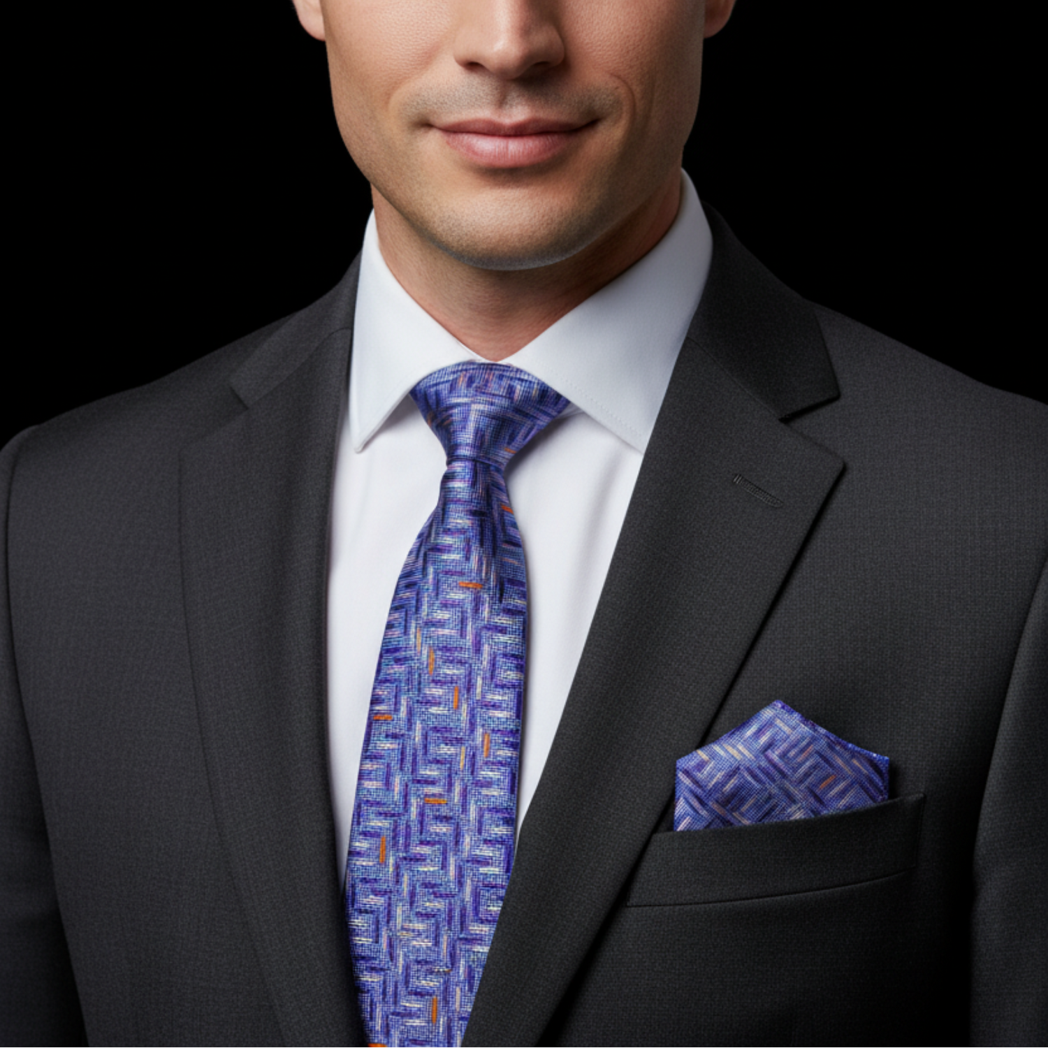 Man wearing a dark suit with a blue patterned tie and pocket square on a black background