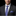 Man wearing a dark suit with a blue patterned tie and pocket square on a black background