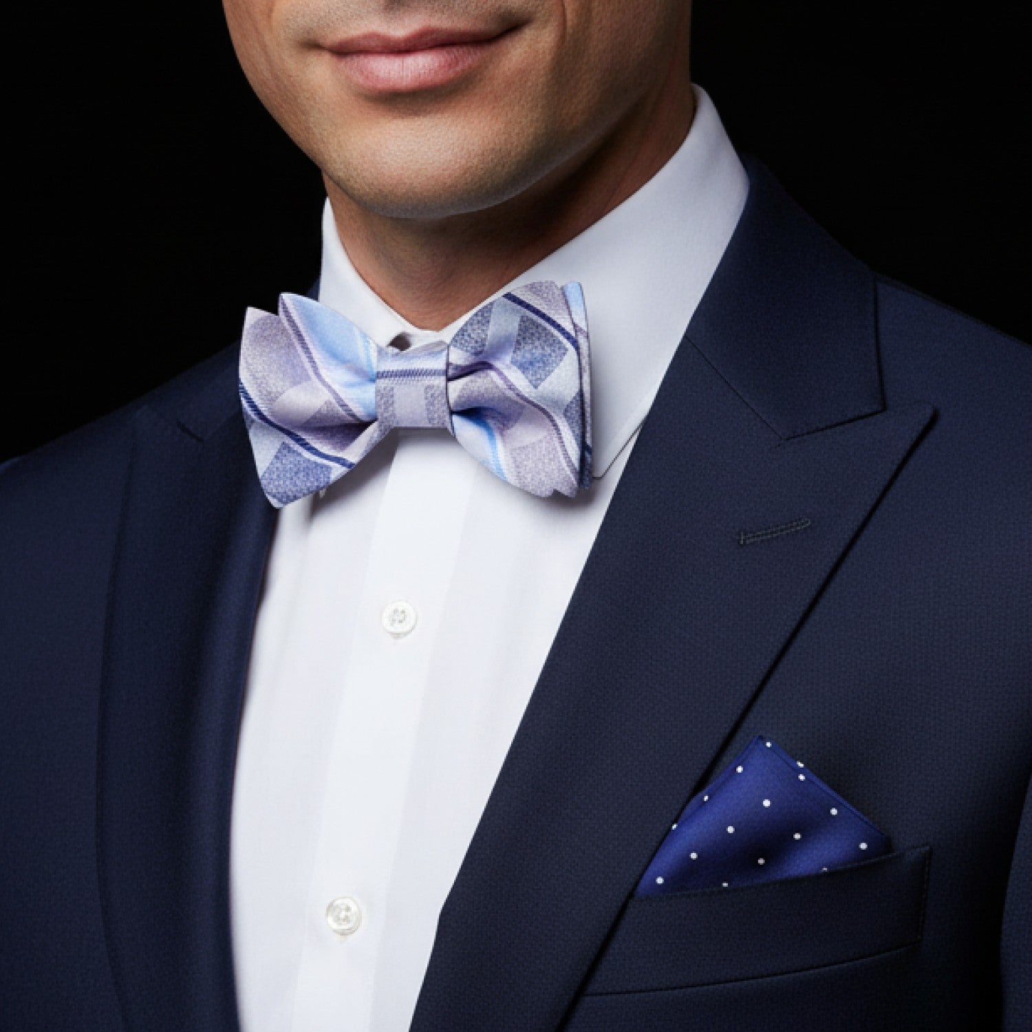 Man wearing a navy suit with a patterned bow tie and pocket square on a black background