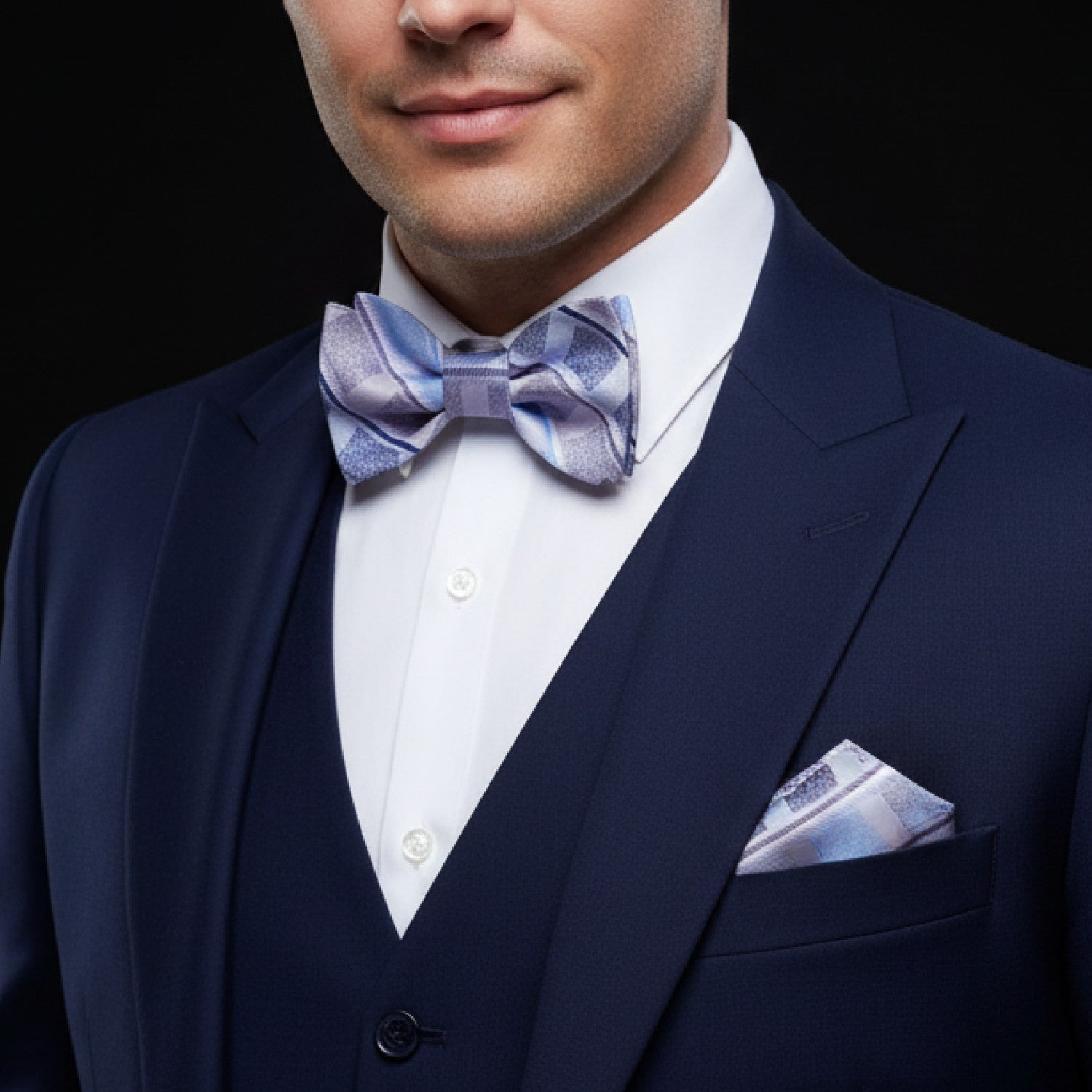 Man wearing a navy suit with a patterned bow tie and pocket square on a black background