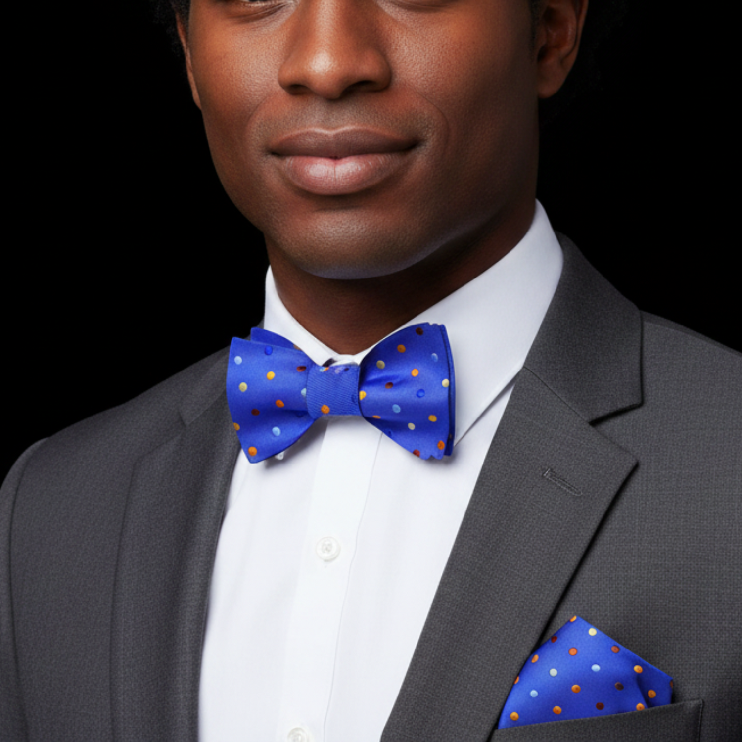 Man wearing a gray suit with a blue bow tie and matching pocket square on a black background