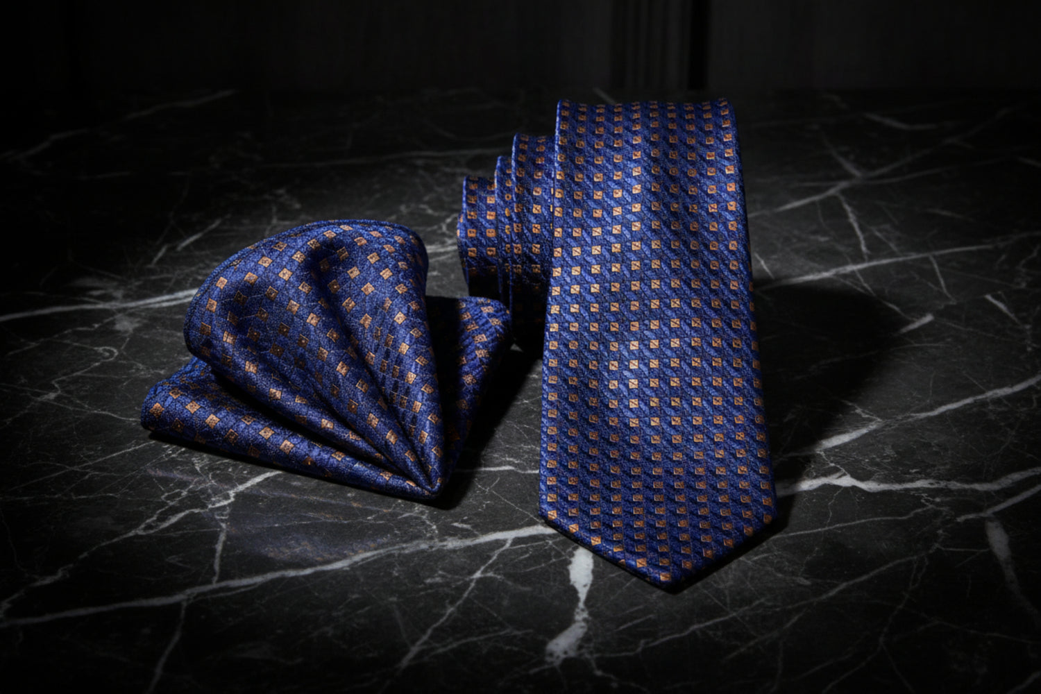 Blue patterned tie and pocket square on a dark marble surface