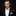 Man wearing a black suit with a yellow bow tie and pocket square on a dark background