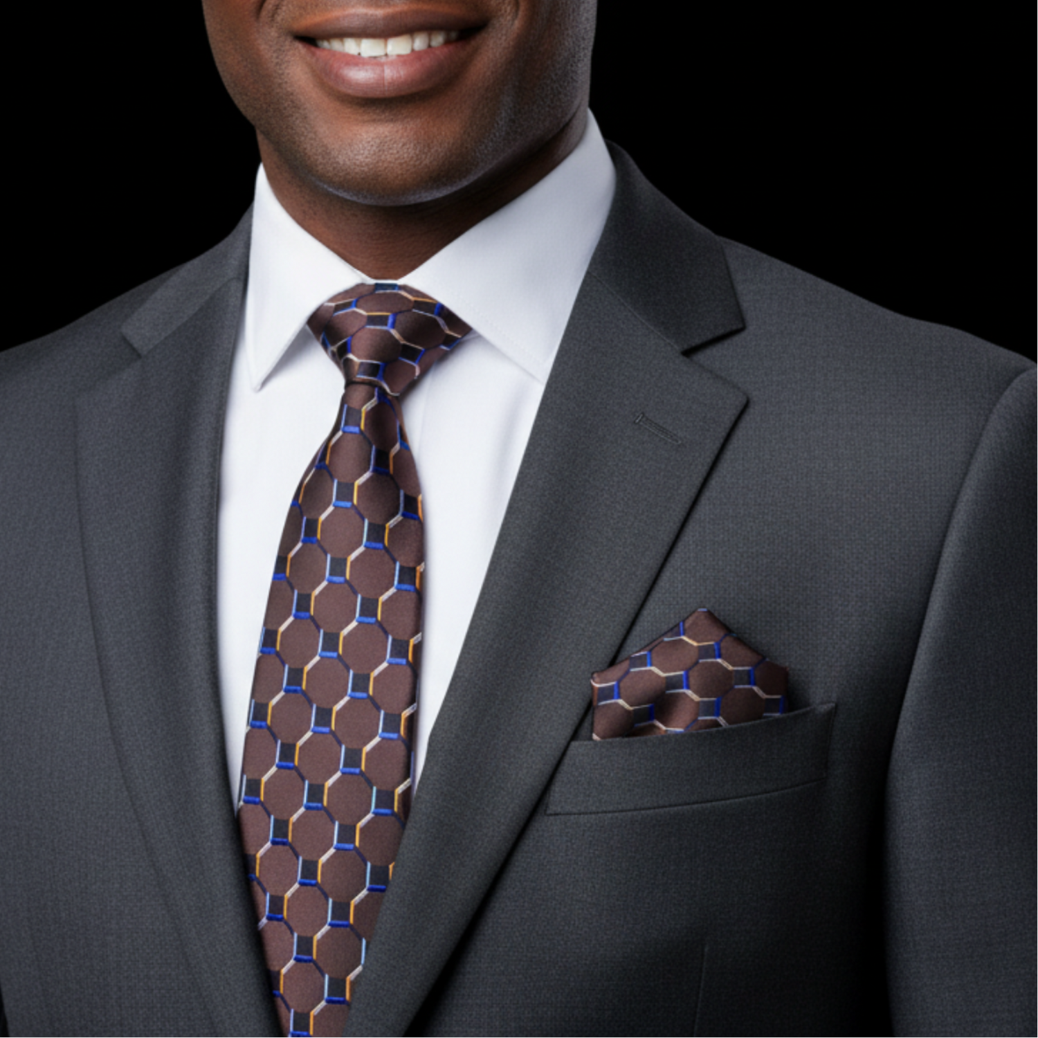 Man wearing a gray suit with a patterned brown tie and pocket square on a black background