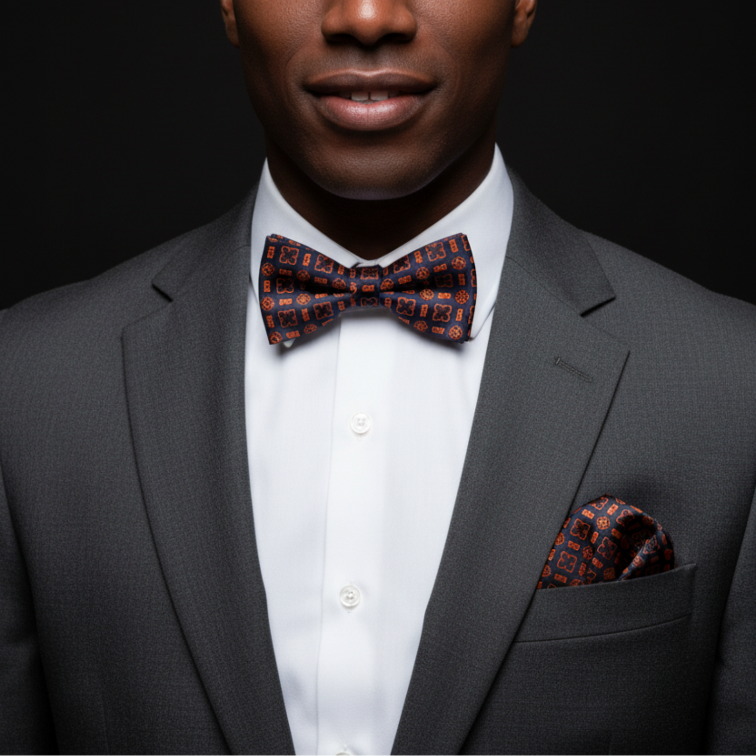 Man wearing a gray suit with a patterned bow tie and pocket square on a black background