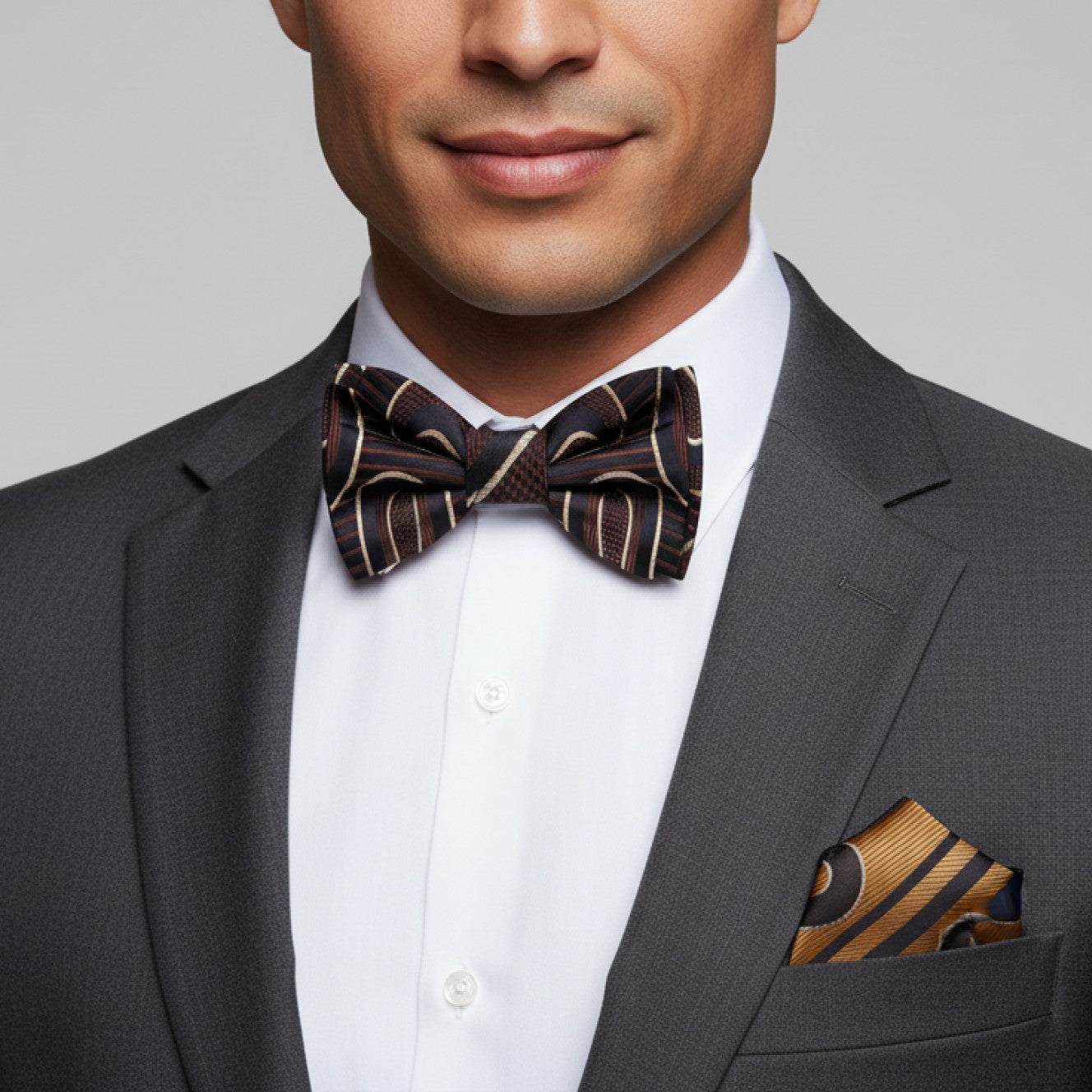 Man wearing a gray suit with a patterned bow tie and pocket square on a gray background