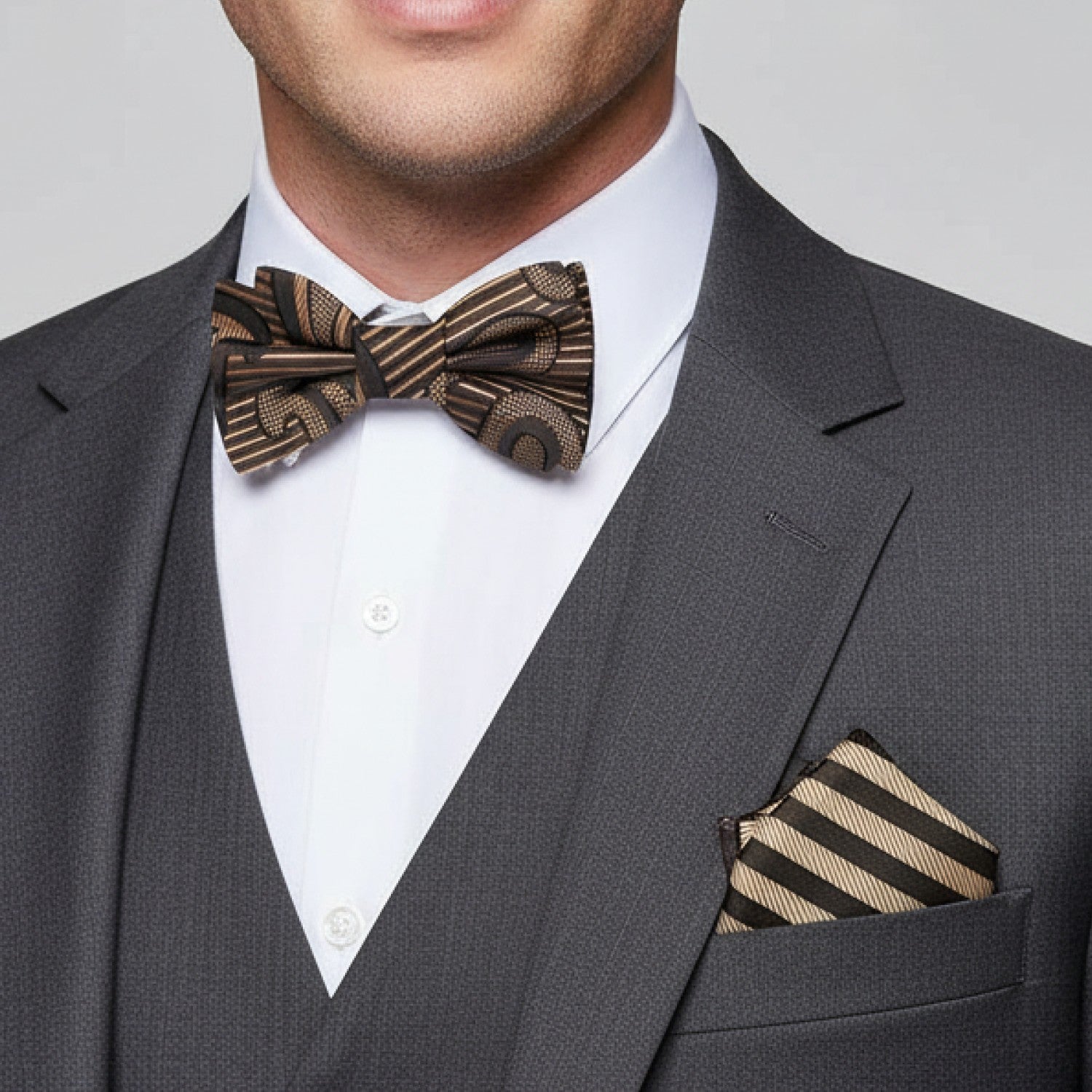 Man wearing a gray suit with a brown and gold striped bow tie and pocket square.