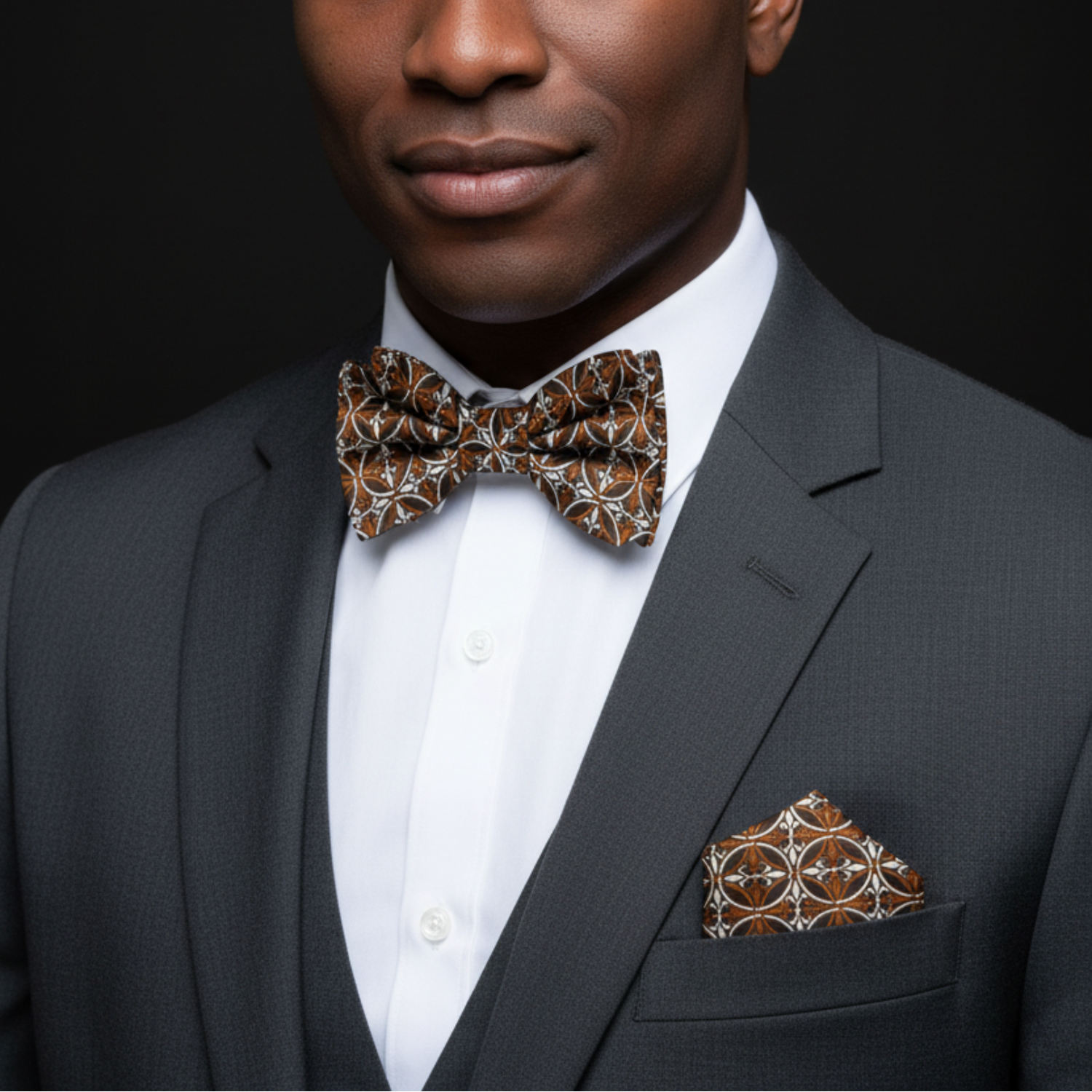Man wearing a gray suit with a patterned bow tie and pocket square on a black background