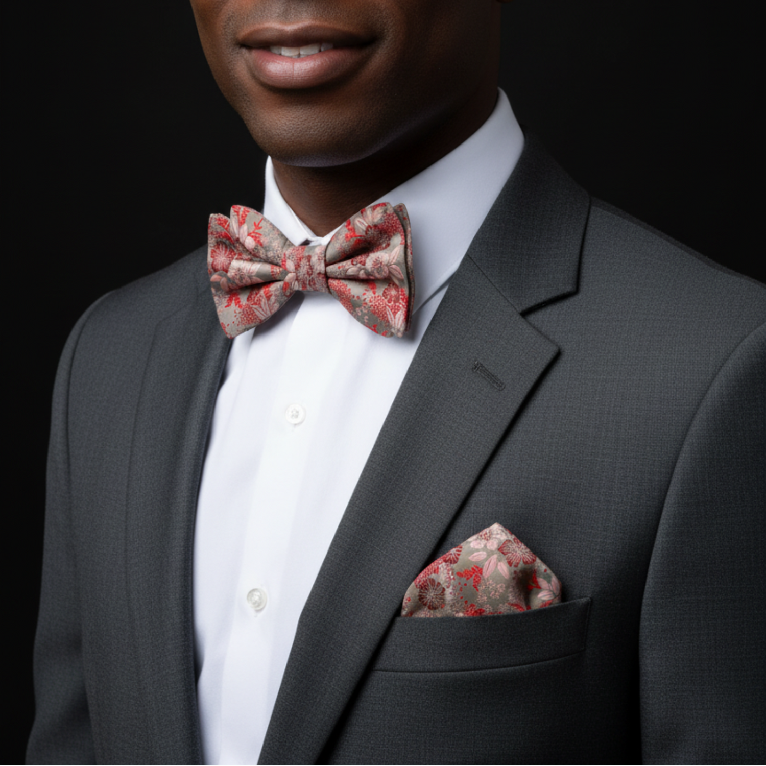 Man wearing a gray suit with a red floral bow tie and pocket square on a black background