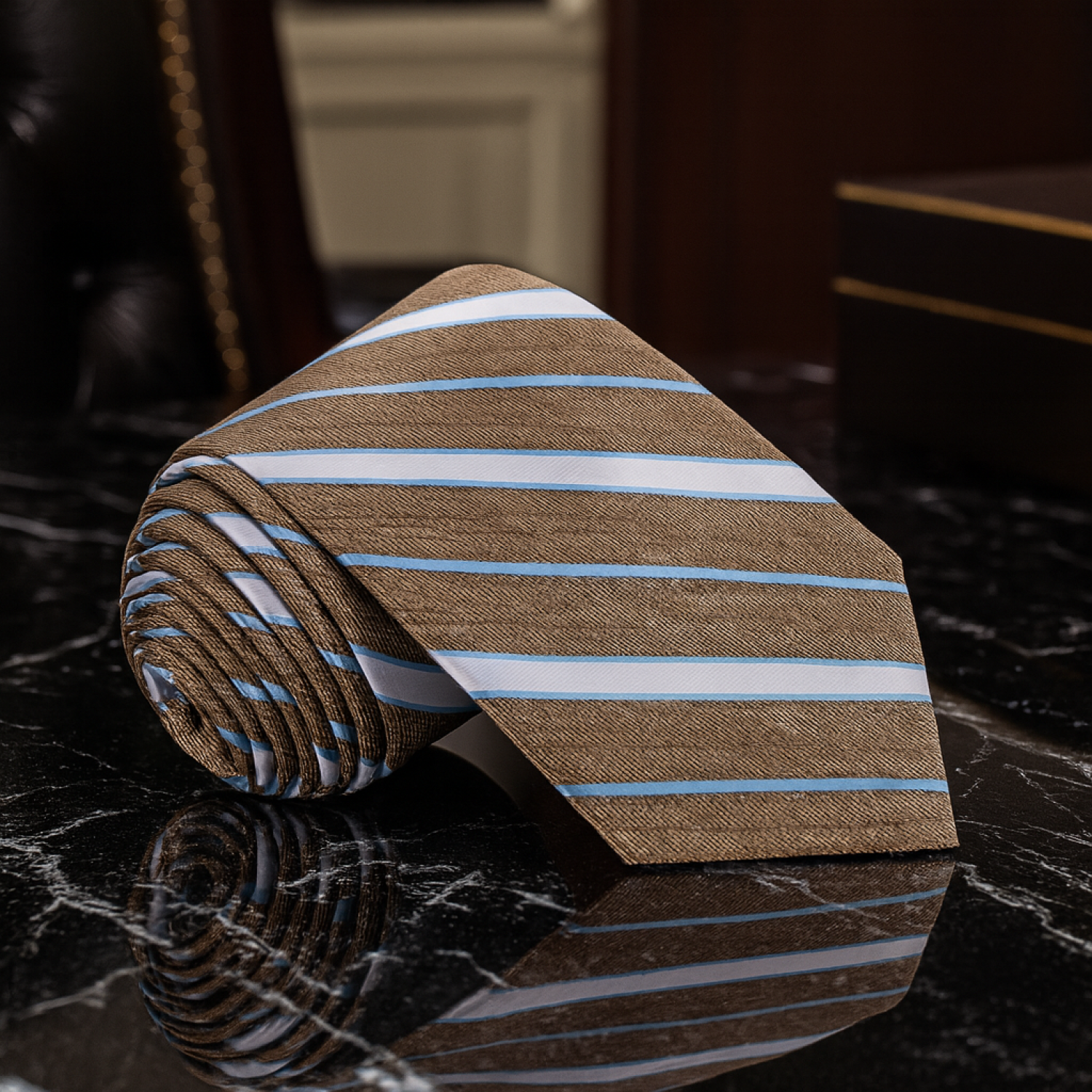 Rolled-up striped tie with brown, blue, and white pattern on a reflective surface.
