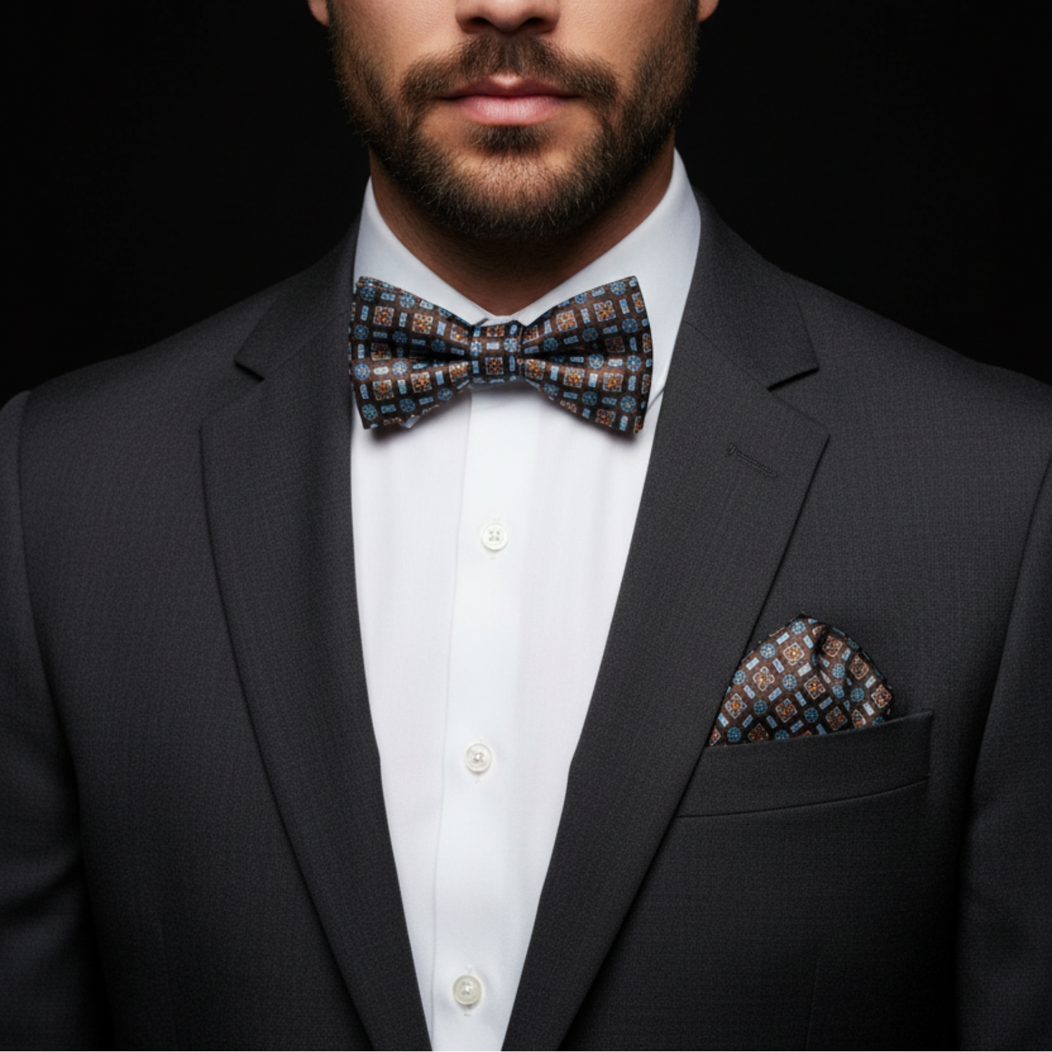 Man wearing a dark gray suit with a patterned bow tie and pocket square on a black background