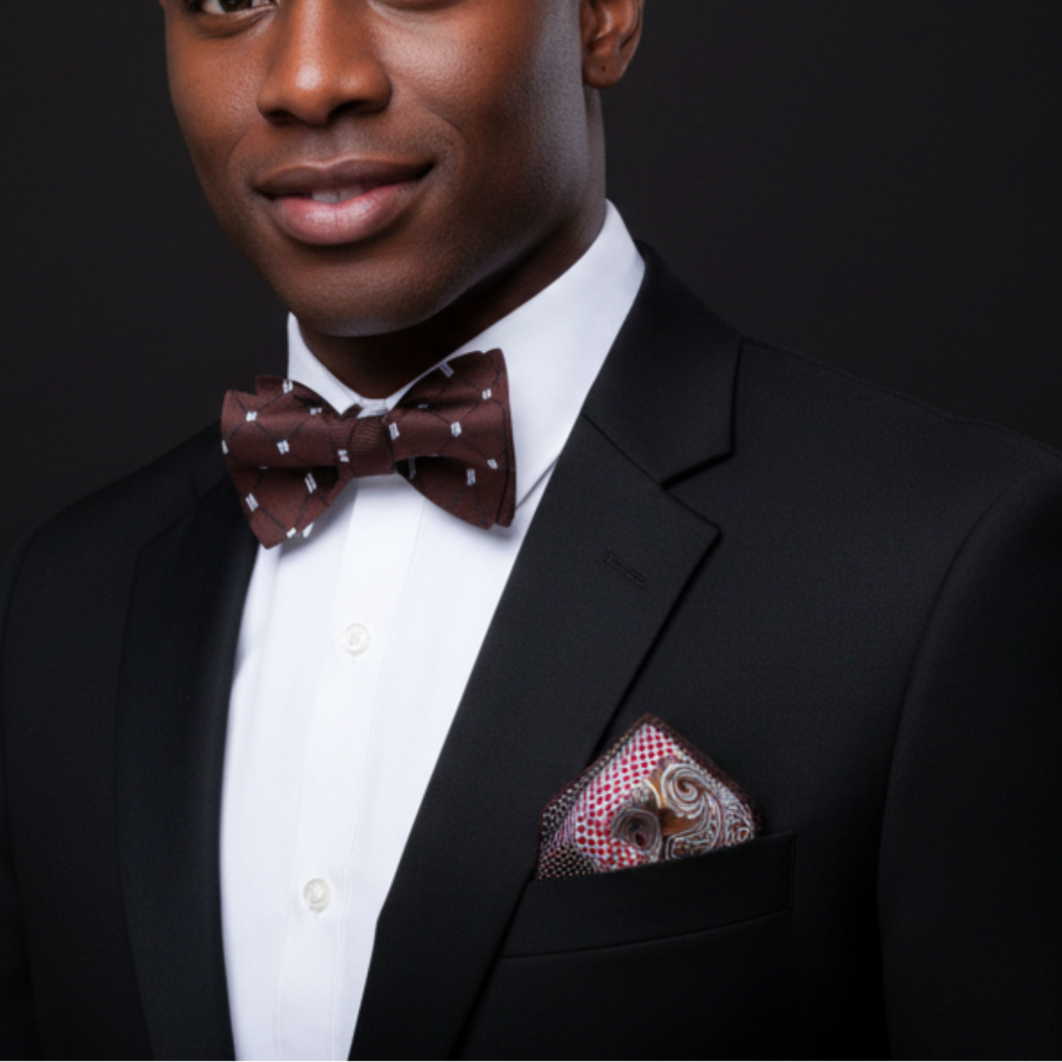 Man wearing a black suit with a polka dot bow tie and patterned pocket square on a dark background