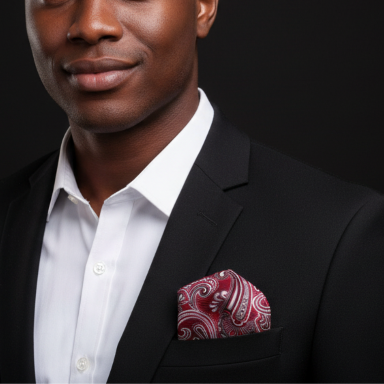 Man wearing a black suit with a white shirt and red paisley pocket square on a dark background