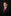 Young boy in a black suit with a red tie and pocket square against a dark background