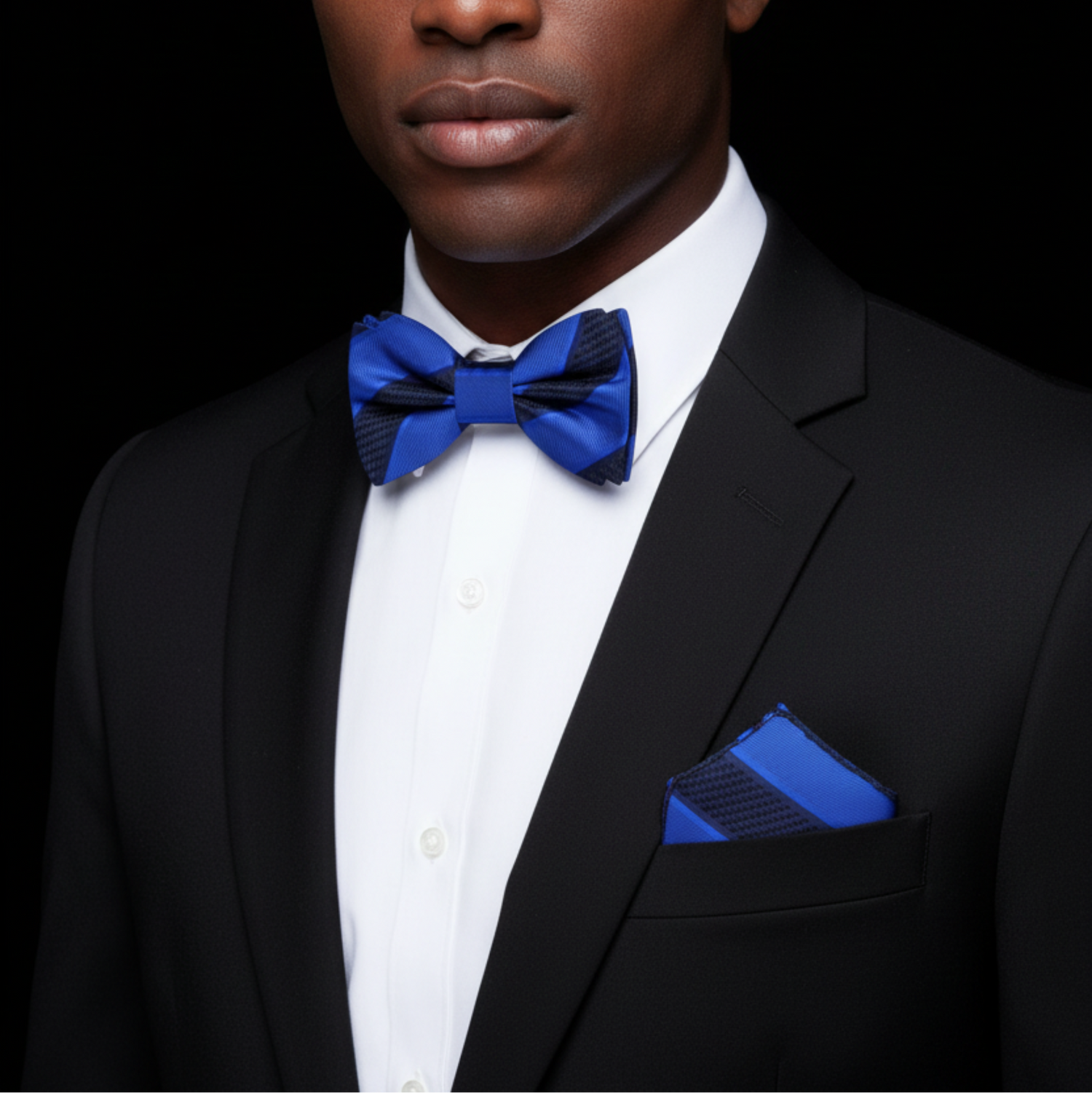 Man wearing a black suit with a blue bow tie and pocket square on a black background