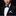 Man wearing a black suit with a blue bow tie and striped pocket square on a black background