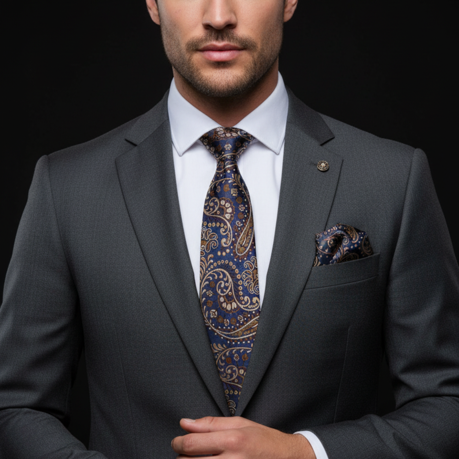 Man wearing a gray suit with a blue and brown paisley patterned tie and pocket square on a black background