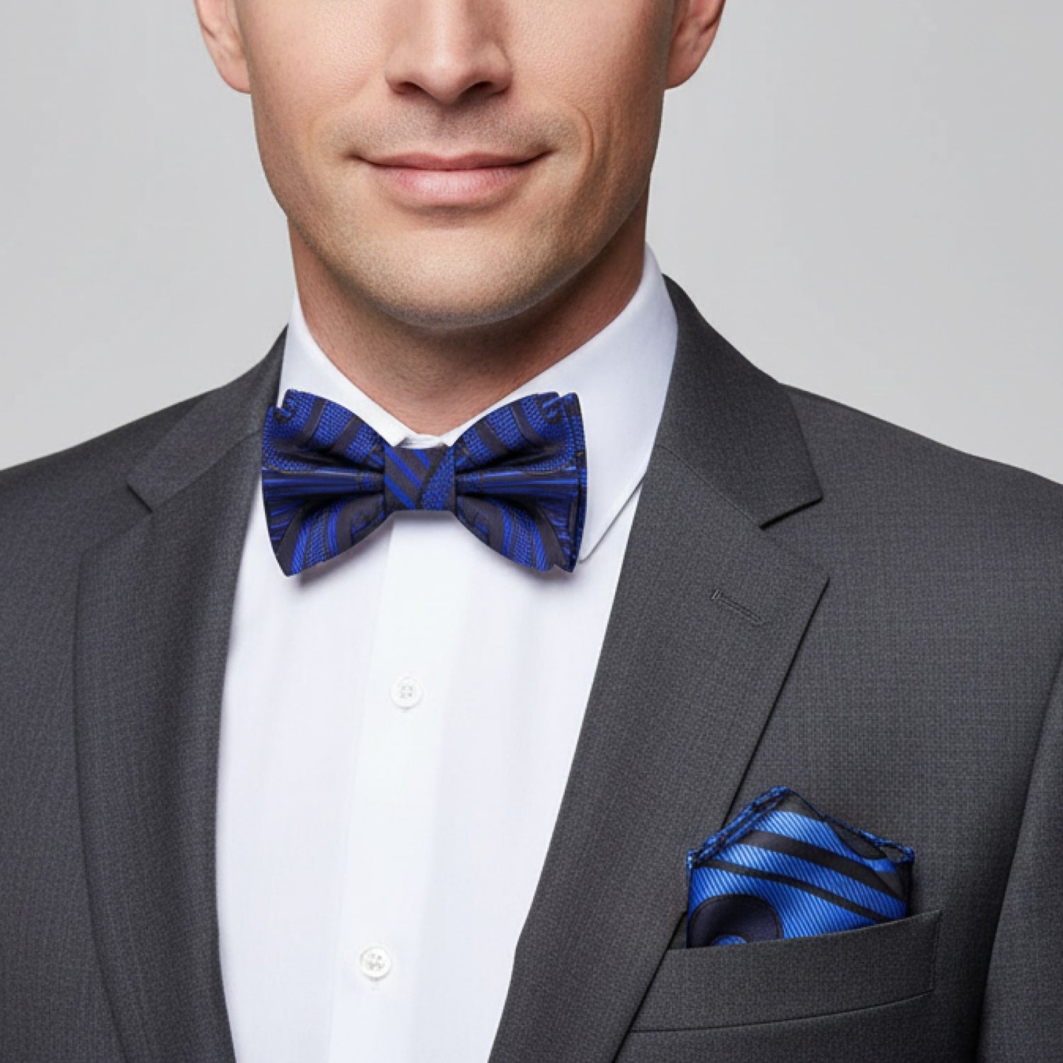 Man wearing a gray suit with a blue bow tie and pocket square on a light gray background